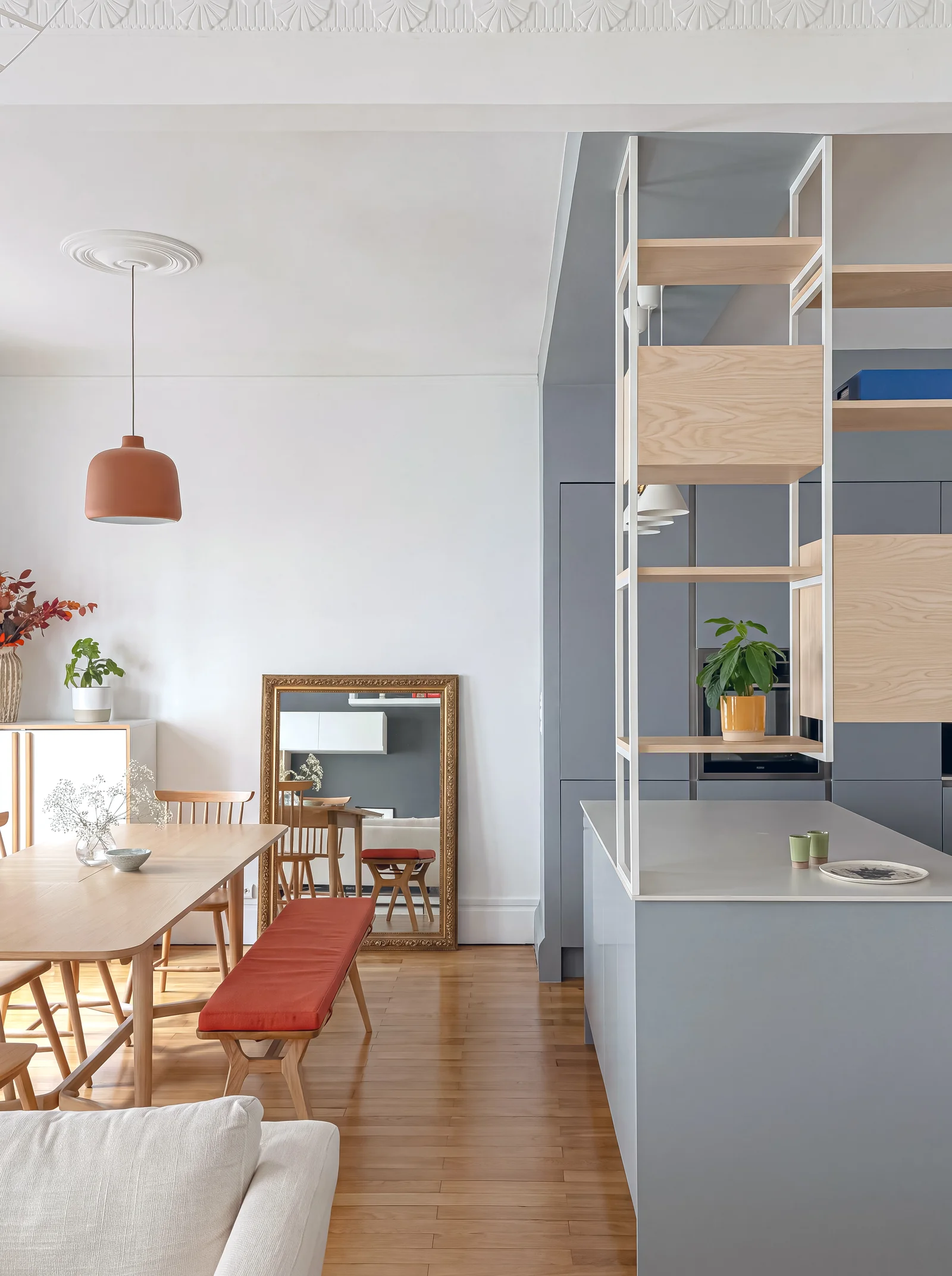 Apartment dining area beside a grey kitchen island with suspended white steel and oak shelving