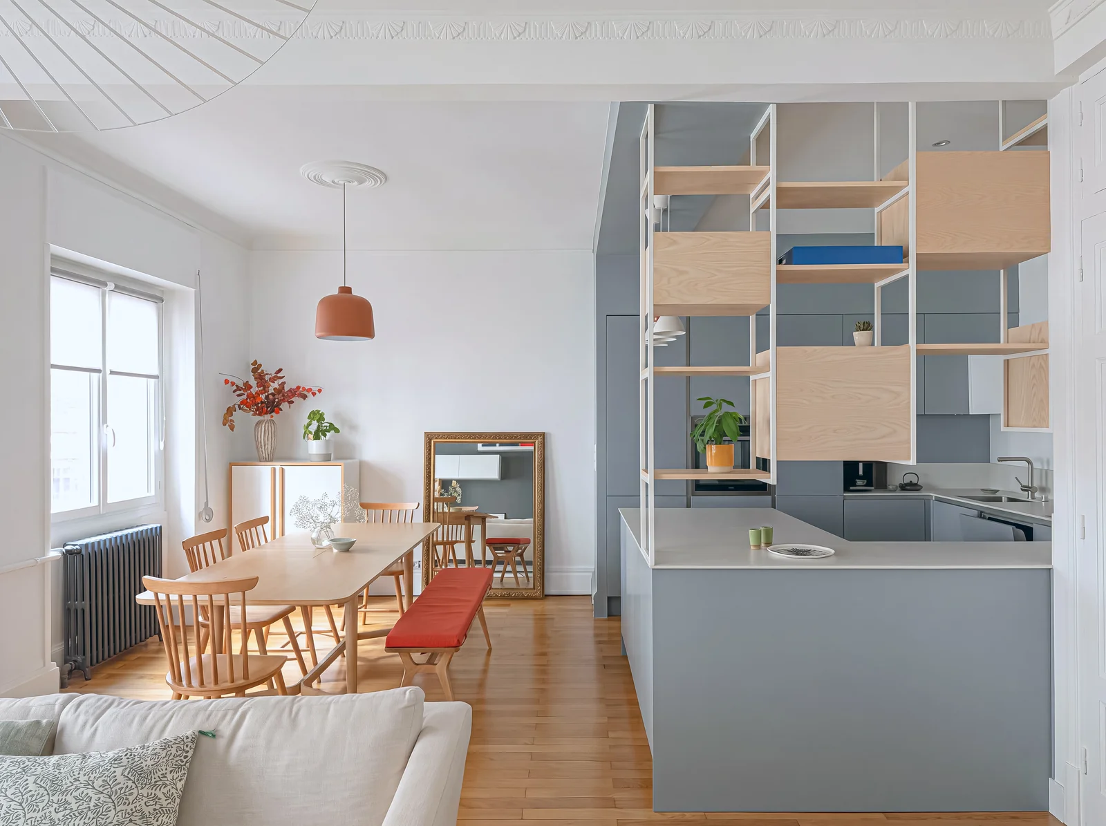 Oak dining table seen past a grey kitchen with steel and oak shelving in a bright apartment