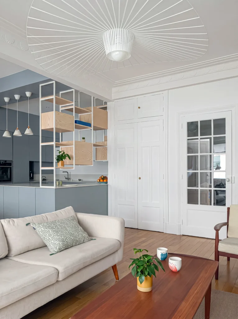 Sitting room with a white sofa looking towards a grey kitchen with oak cubby shelving and glazed doors