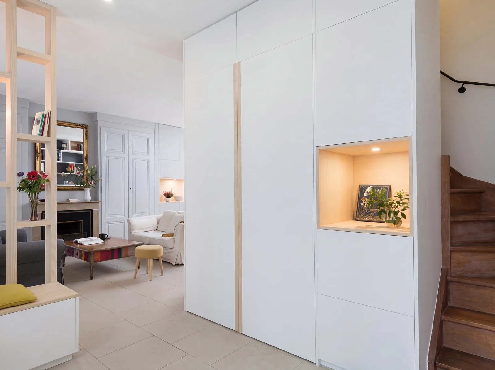 White full-height storage wall with a lit oak-lined niche beside a staircase