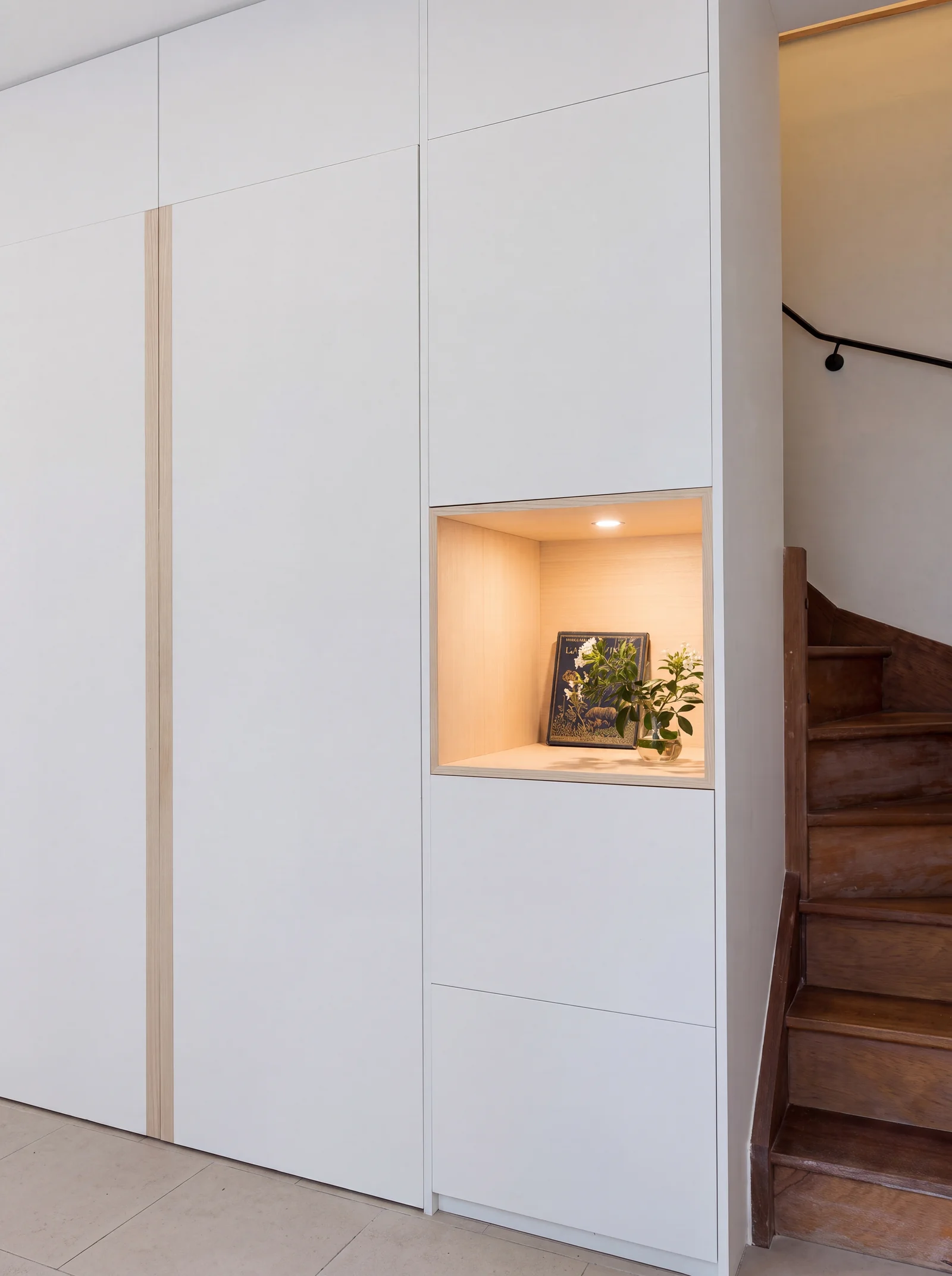 Close-up of a lit oak-lined display niche set into white handleless cupboards beside the stairs