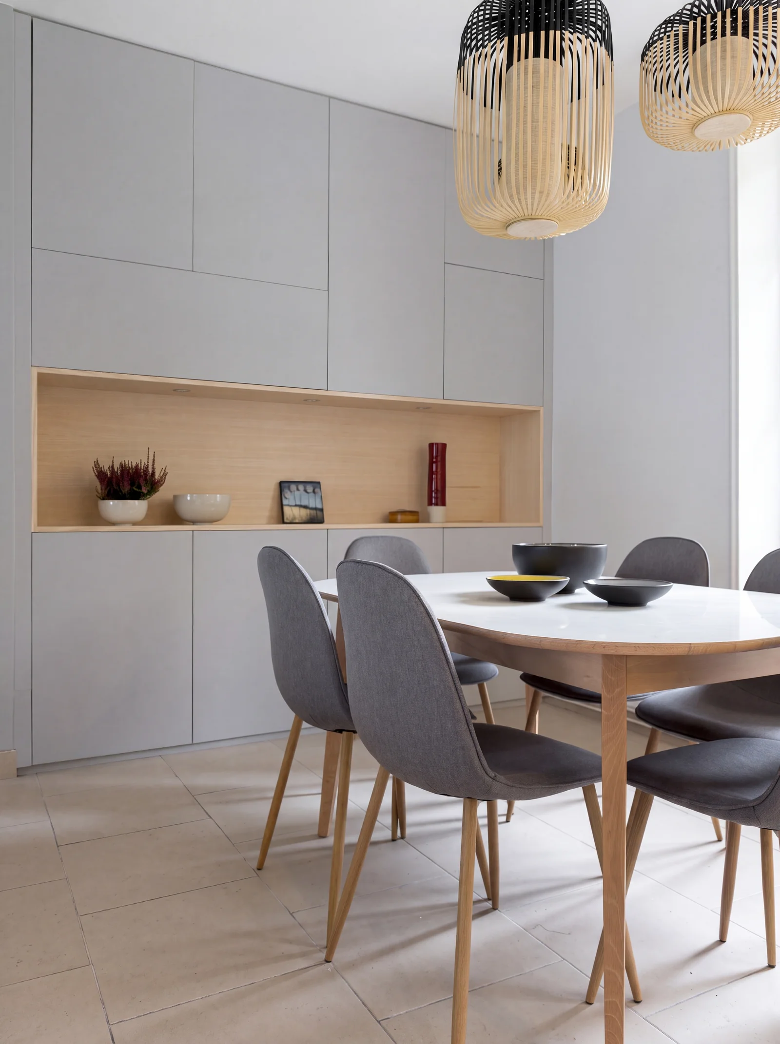 Dining area with pale grey wall cabinets and a lit oak display shelf above a round white table