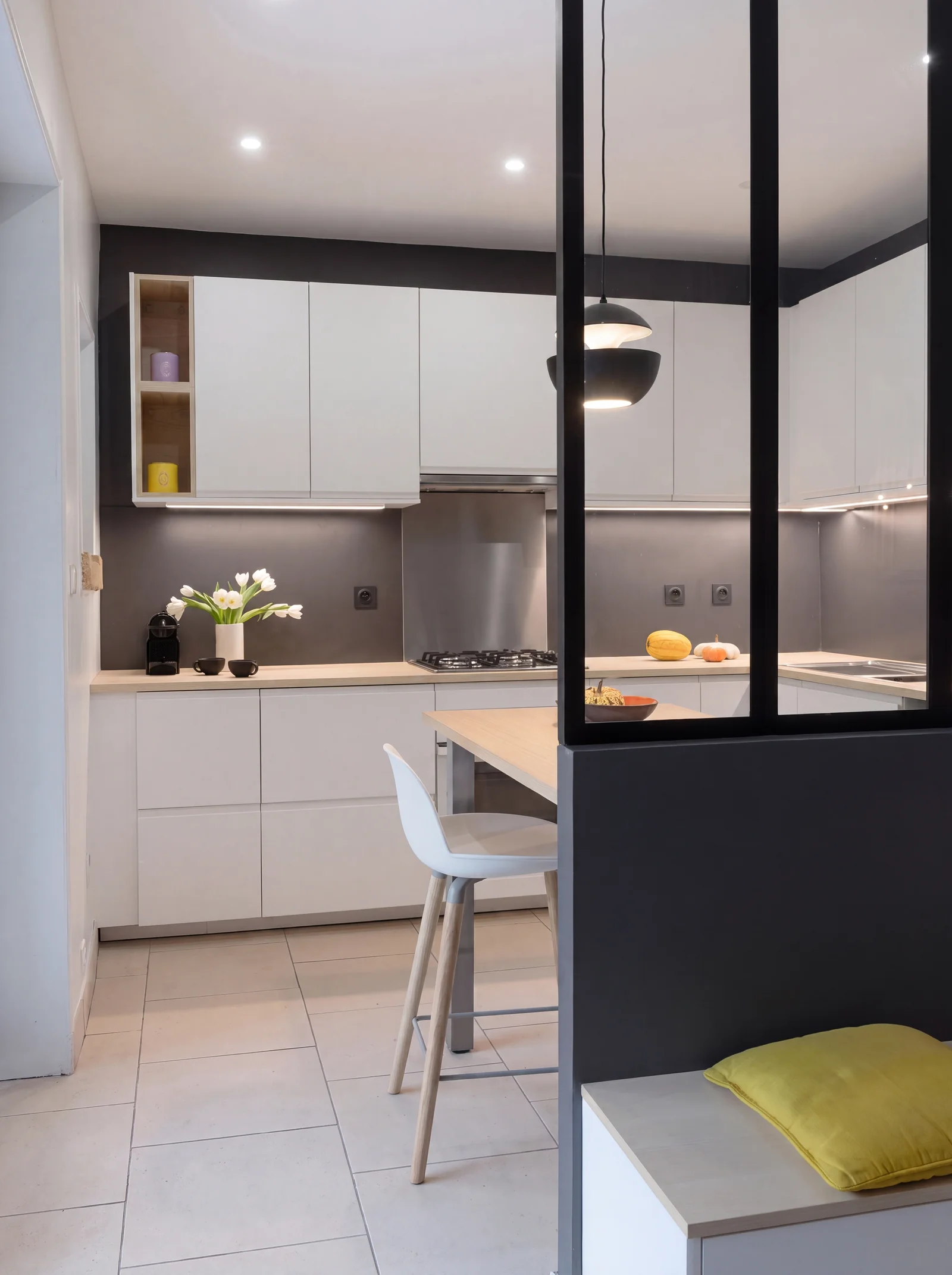 White kitchen with a breakfast bar seen through a black steel-framed glass partition