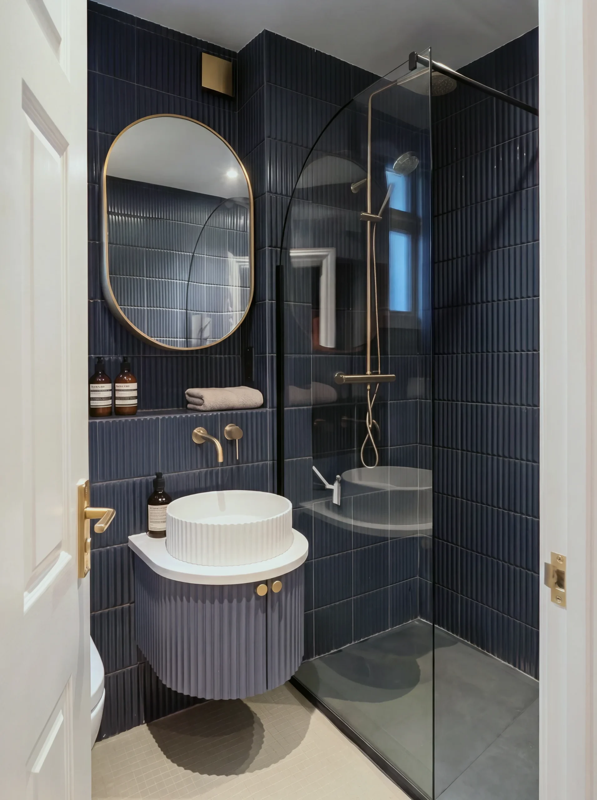 Shower room vanity in Fulham: small bathroom with navy vertical tiles, a curved navy vanity with a white basin and a brass oval mirror