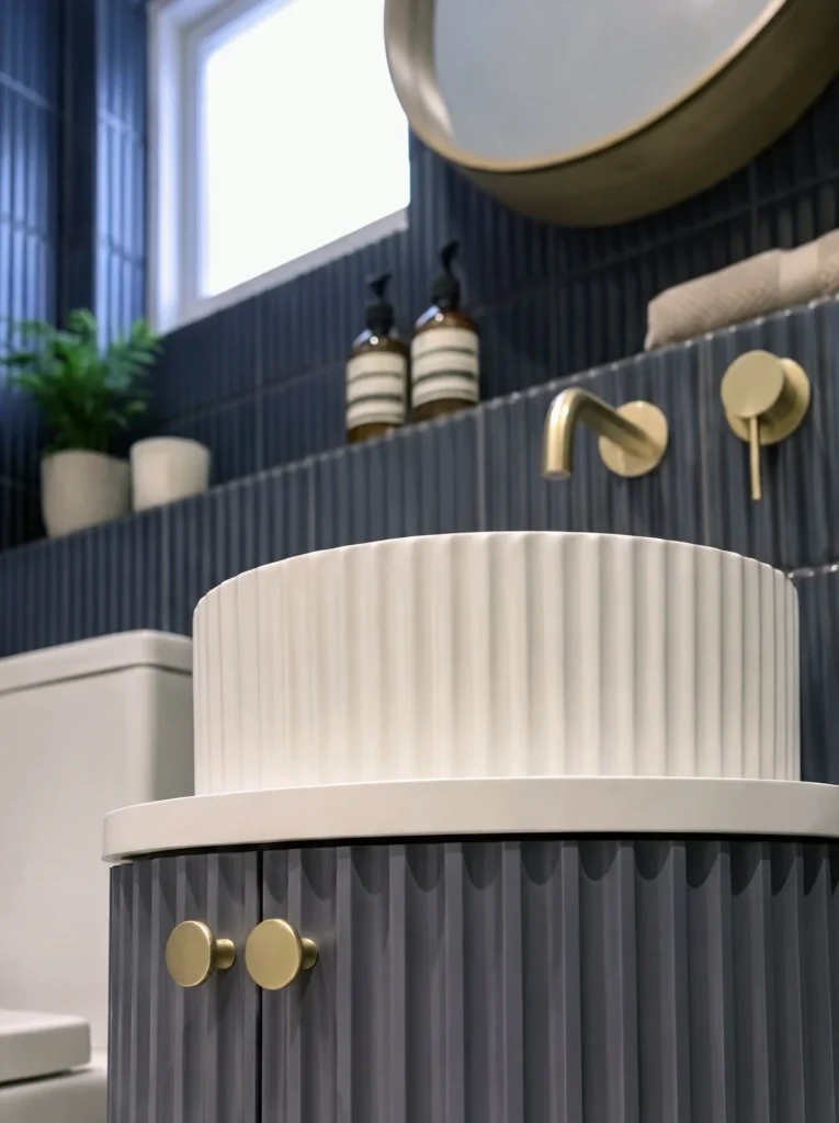 Fluted white basin on a ribbed navy vanity with brass knobs and a brass wall tap
