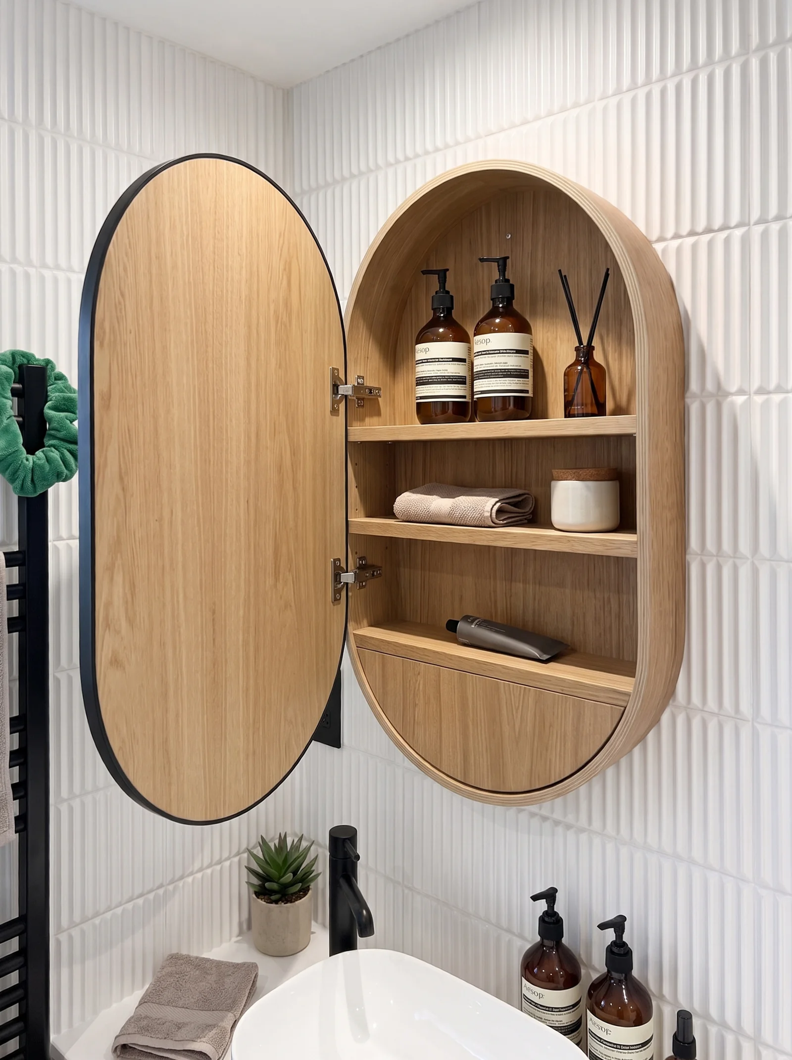 Oval oak mirror cabinet opened to show shelves of toiletries above a white basin