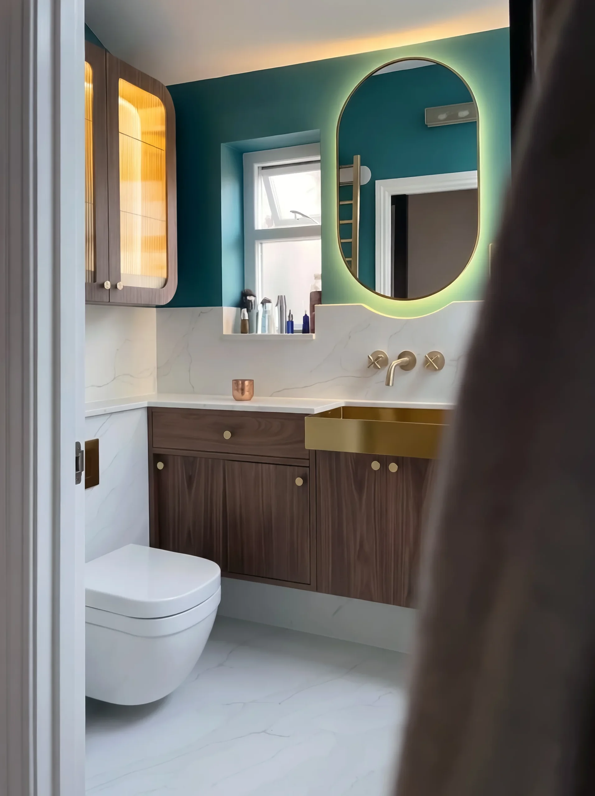 Walnut vanity in Notting Hill: walnut bathroom vanity with a brass basin and a lit oval mirror on a teal wall in Fulham