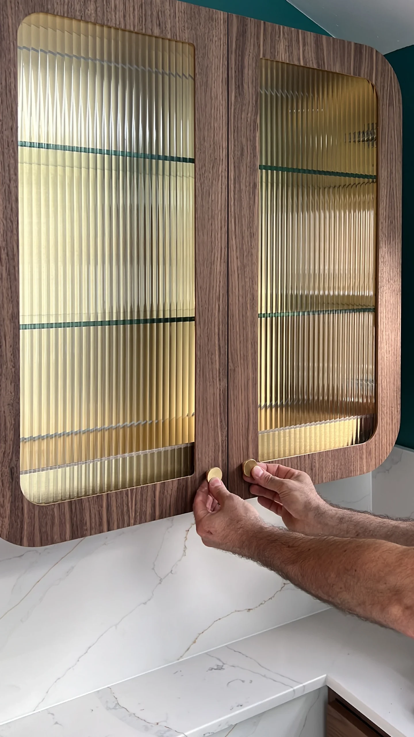 Hand opening a walnut wall cabinet with reeded glass doors