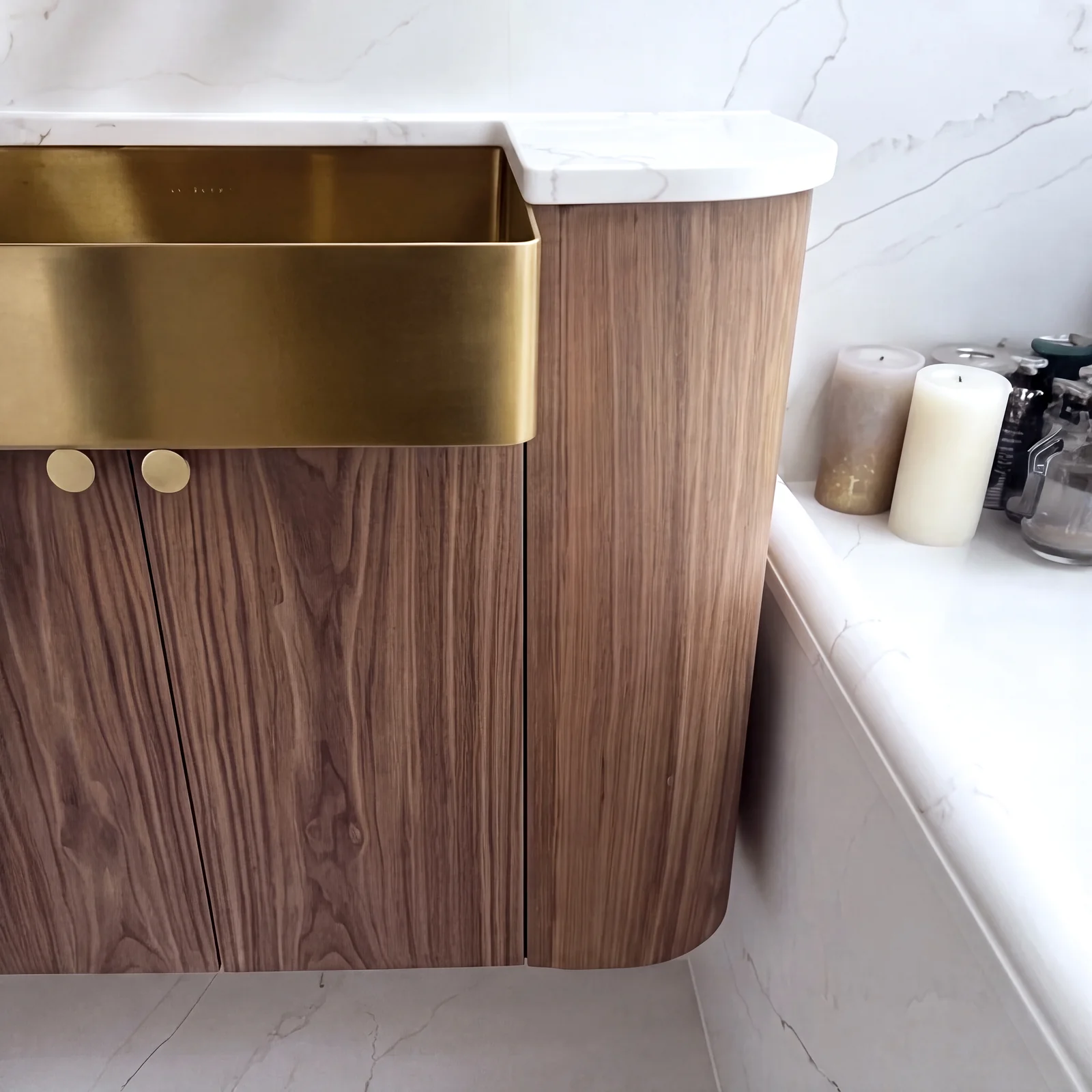 Close-up of a rounded walnut vanity end with a brass apron-front sink and marble top