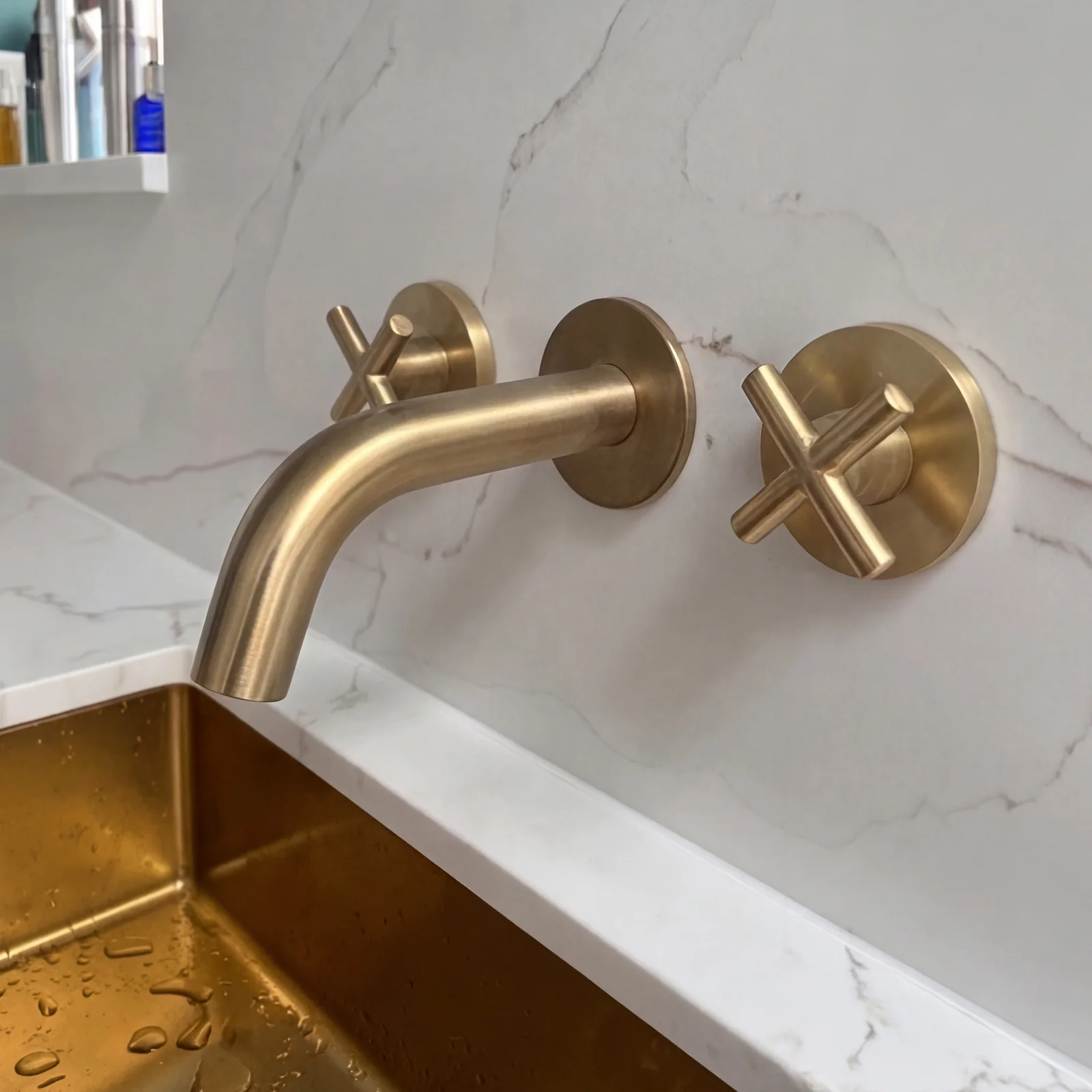 Close-up of a brushed brass wall tap with cross handles above a brass basin