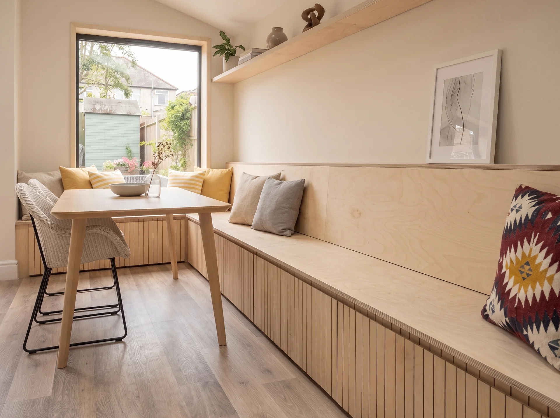 Dining banquette in Bromley: birch plywood dining banquette with a slatted base, cushions and a light wood table by a window