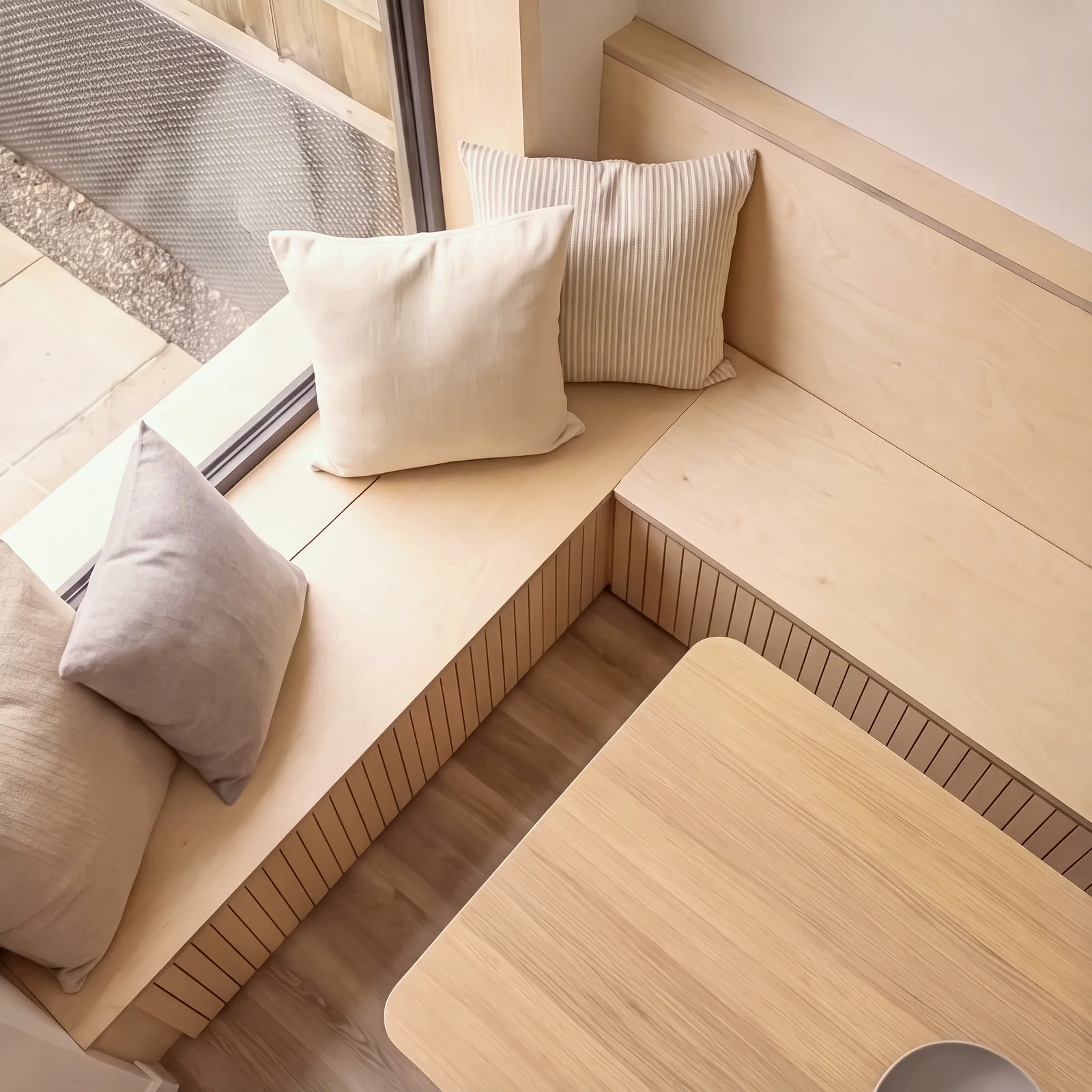 Overhead view of a corner birch ply banquette with cushions and a light wood table