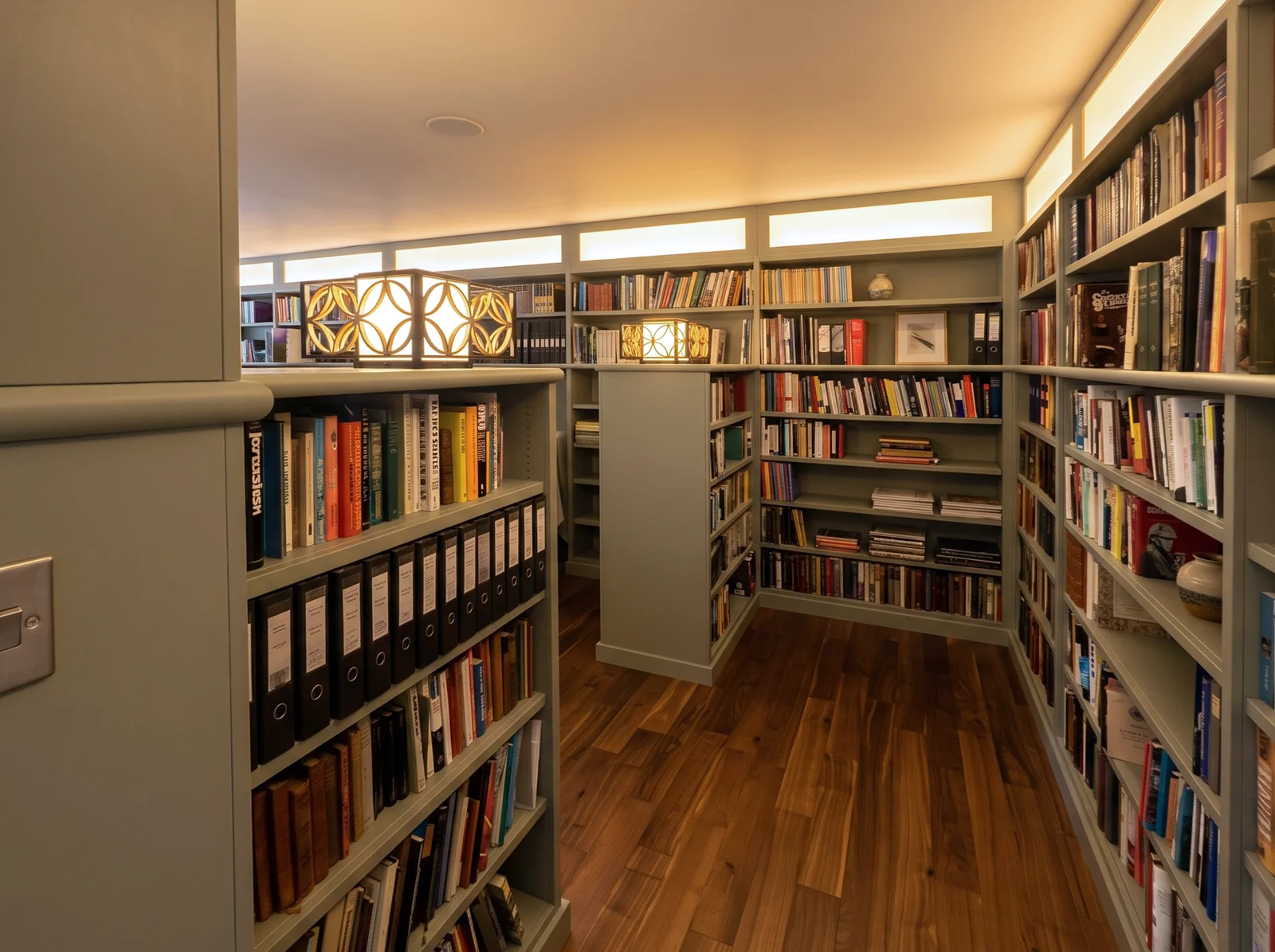 Sage green floor-to-ceiling bookshelves lining a library corridor with geometric table lamps