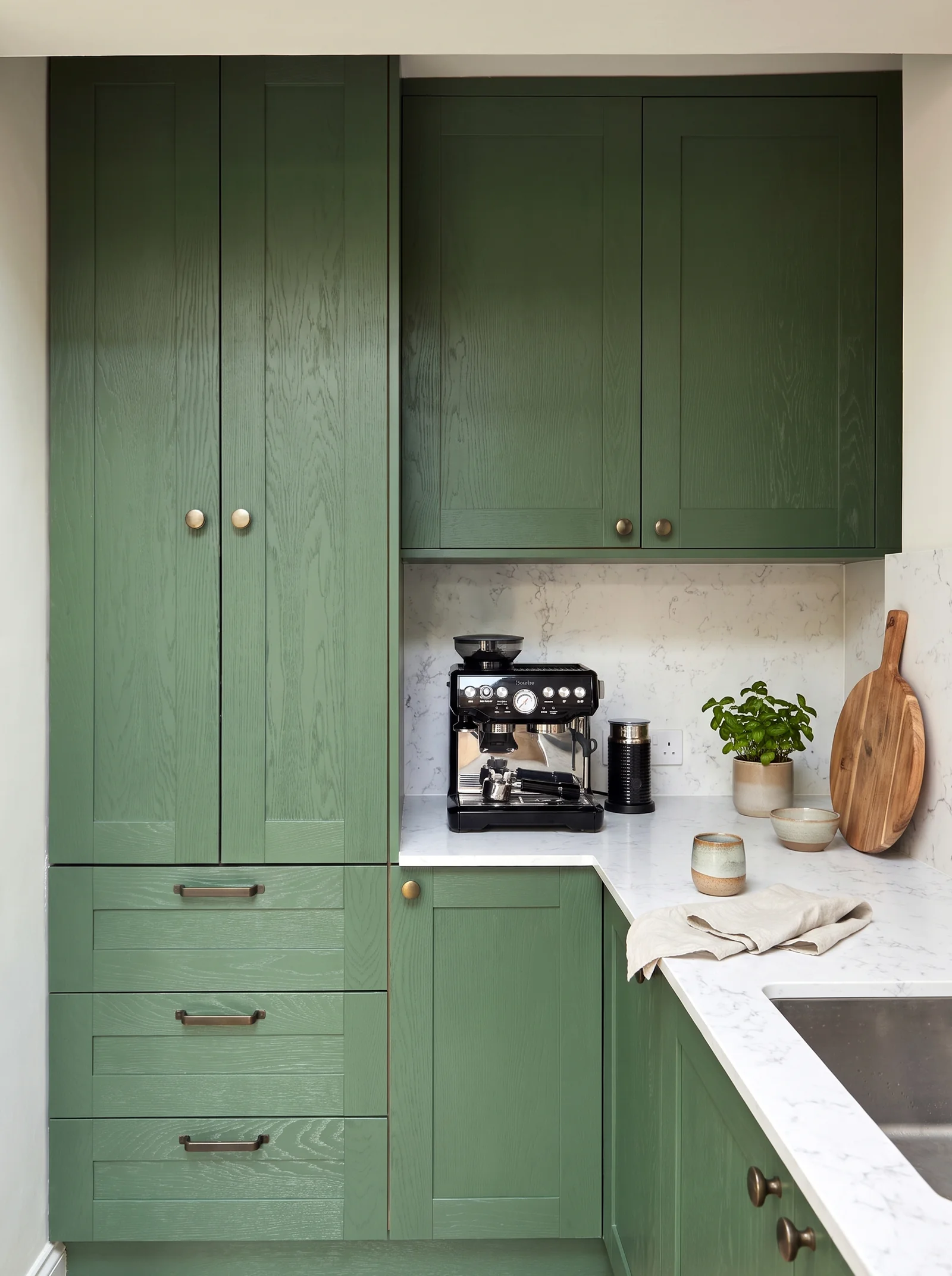 Green painted kitchen corner with full-height cupboards, deep drawers and a white quartz worktop