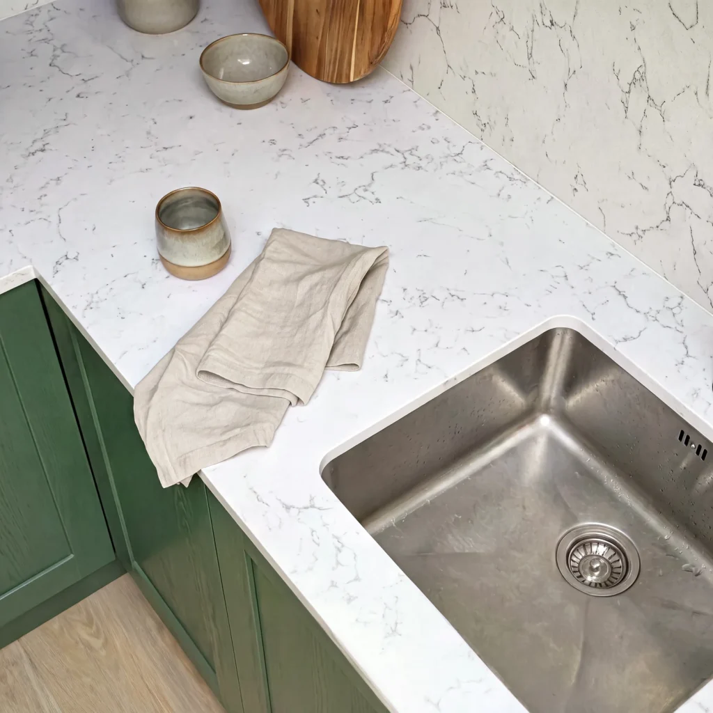 Close-up of an undermount steel sink in a white marble-effect worktop over green cabinets