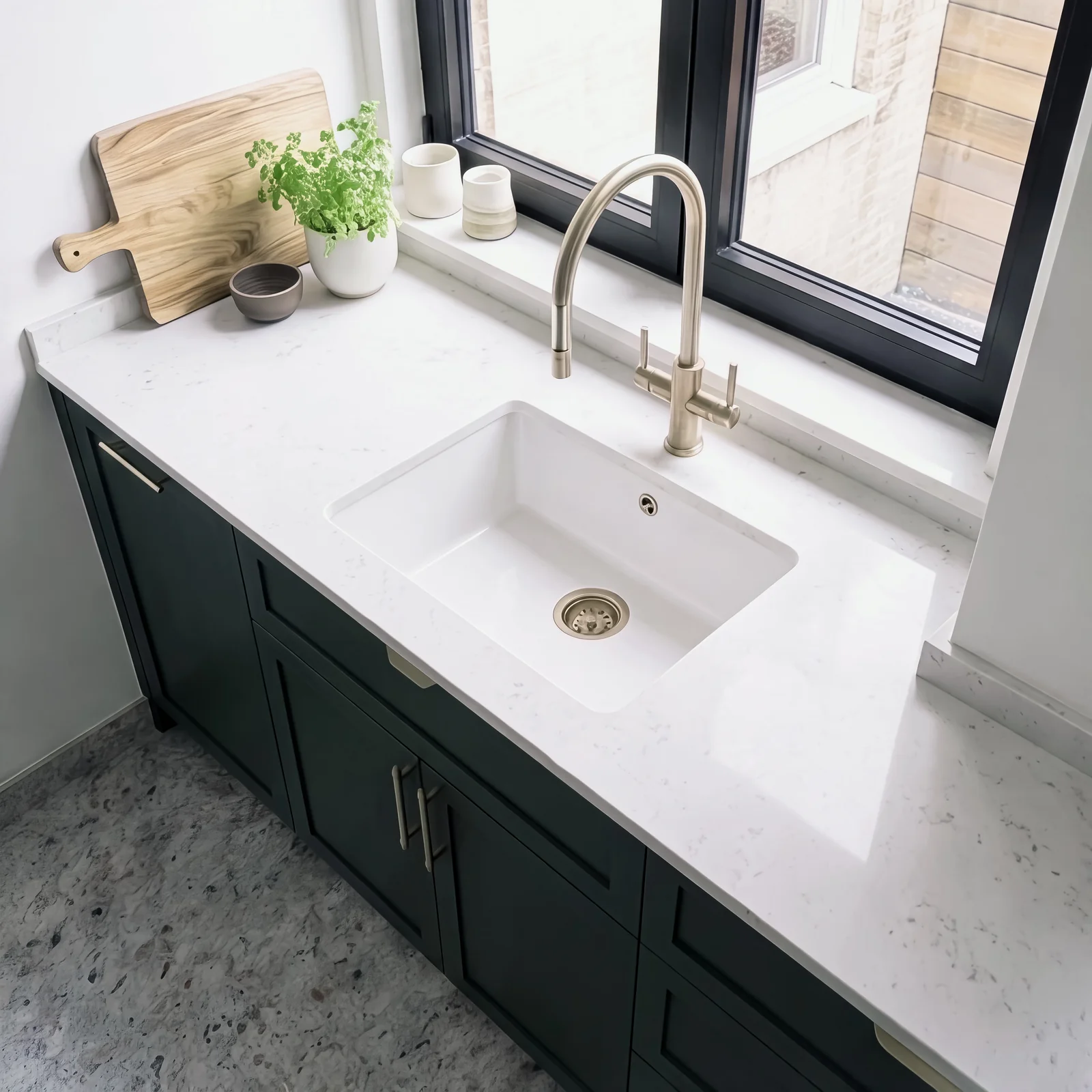 White undermount sink with a brass tap on a white quartz worktop over dark green cabinets