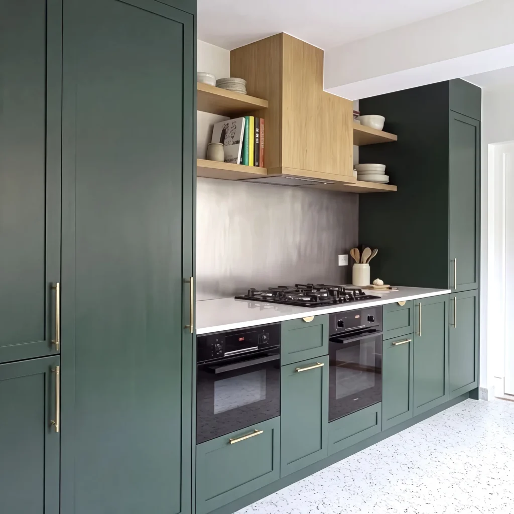 Tall dark green larder cupboard beside a run of green shaker units, ovens and oak shelving