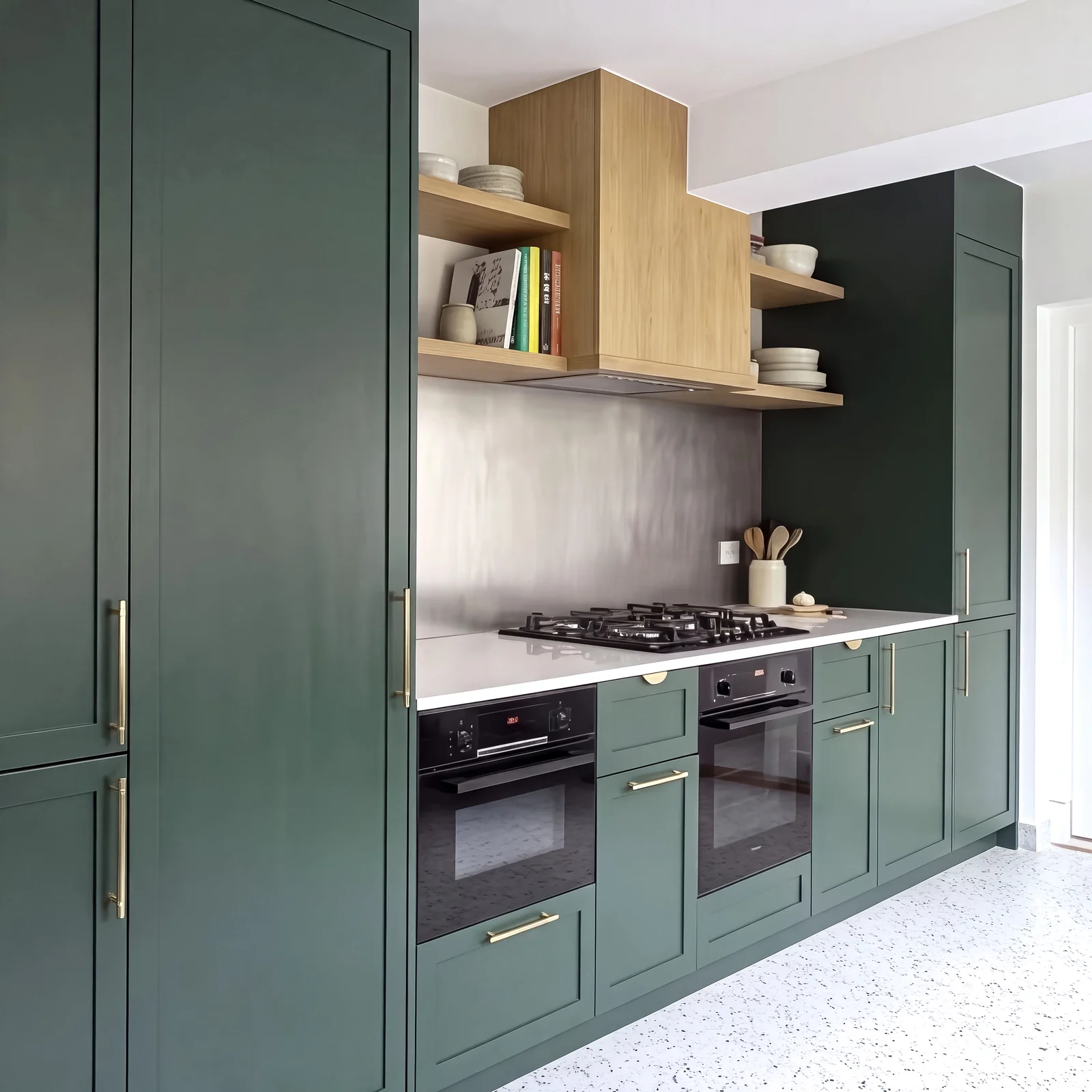 Tall dark green larder cupboard beside a run of green shaker units, ovens and oak shelving