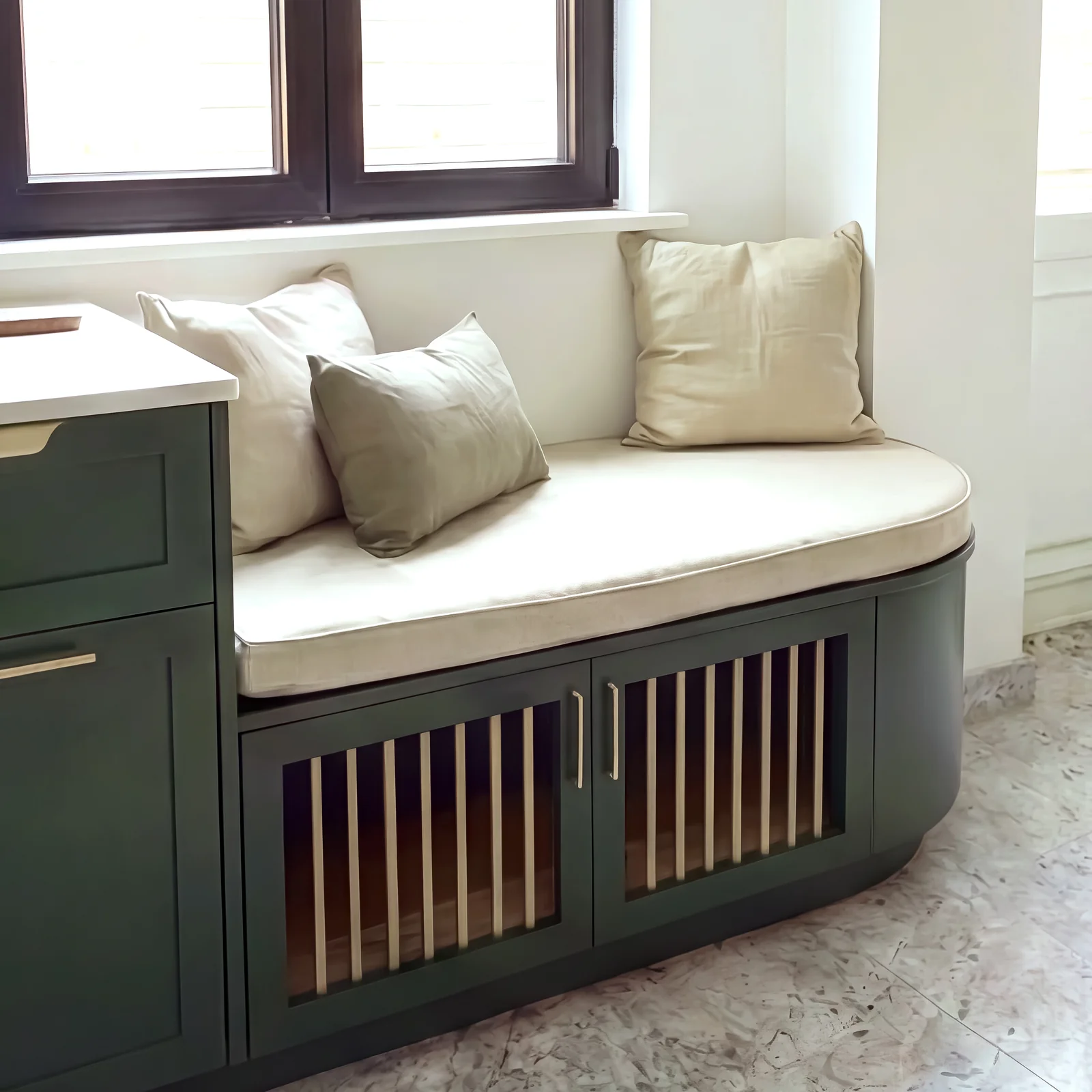 Curved cushioned window seat with slatted dog bed doors at the end of a green kitchen