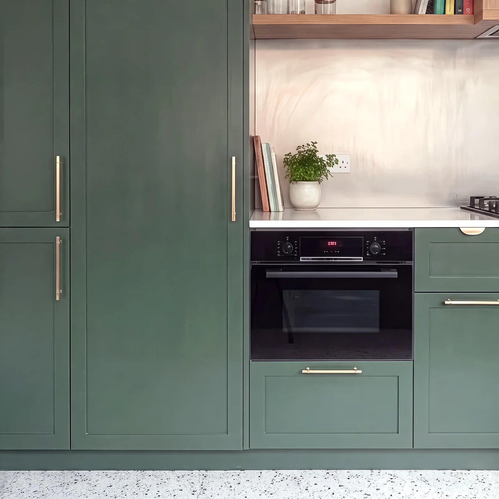 Tall dark green shaker larder doors with brass handles beside a built-in oven and oak shelf