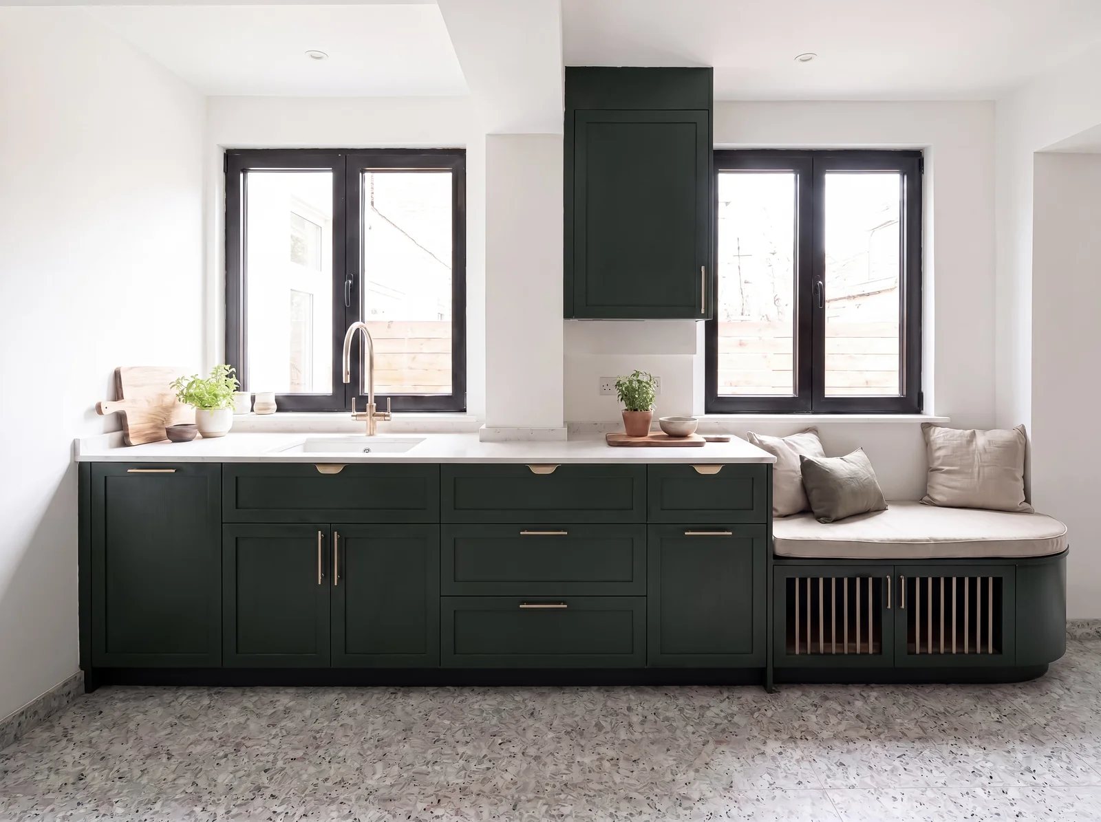 Dark green shaker kitchen under two windows, with a cushioned window seat over a slatted dog bed