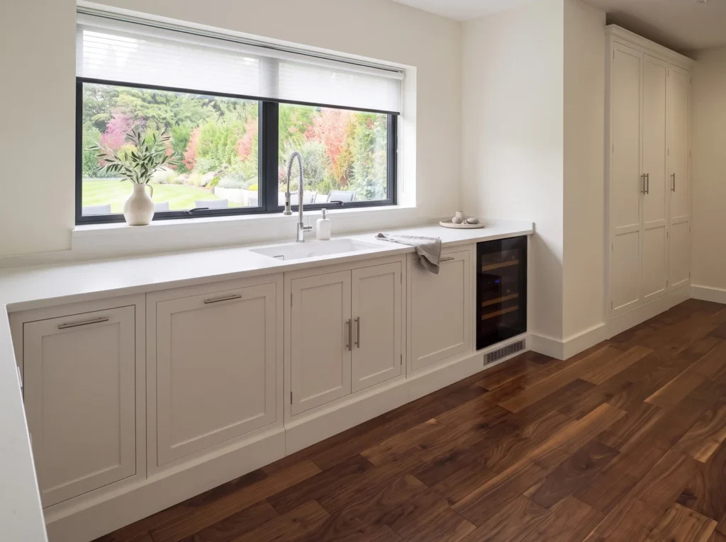 Pale grey in-frame sink run under a wide window with an integrated wine cooler in Bickley