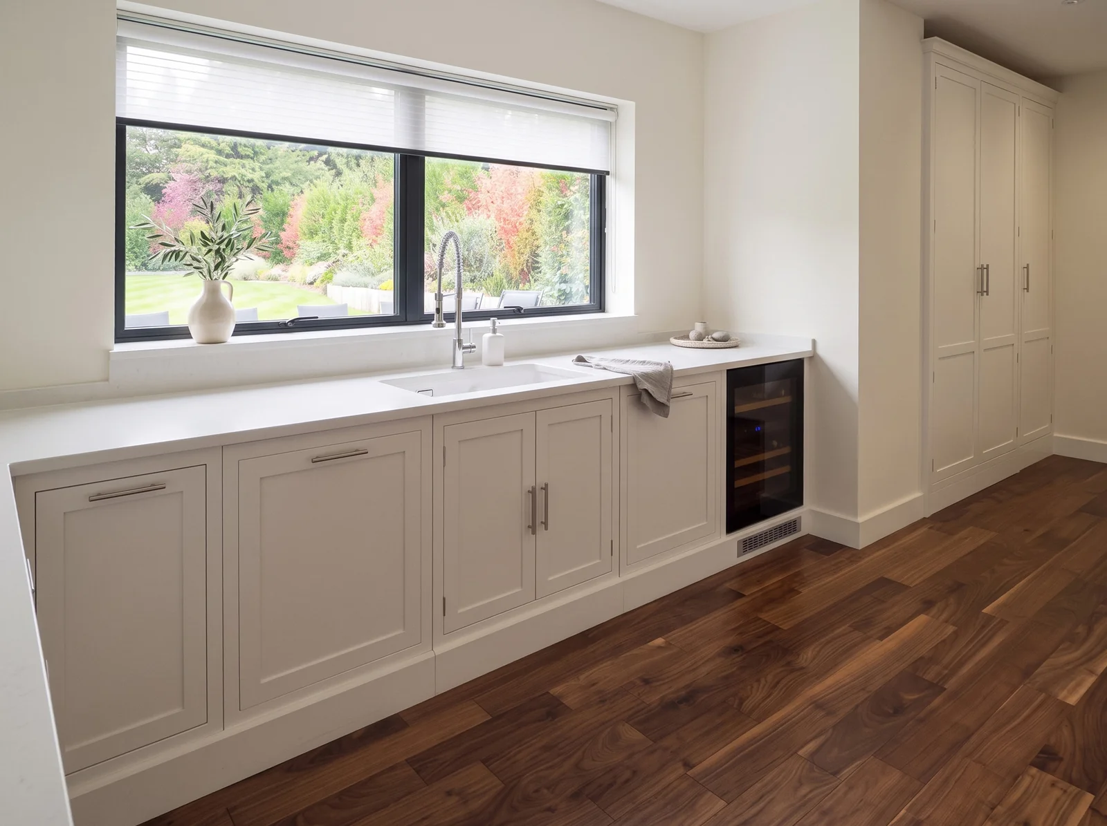 Pale grey in-frame sink run under a wide window with an integrated wine cooler in Bickley