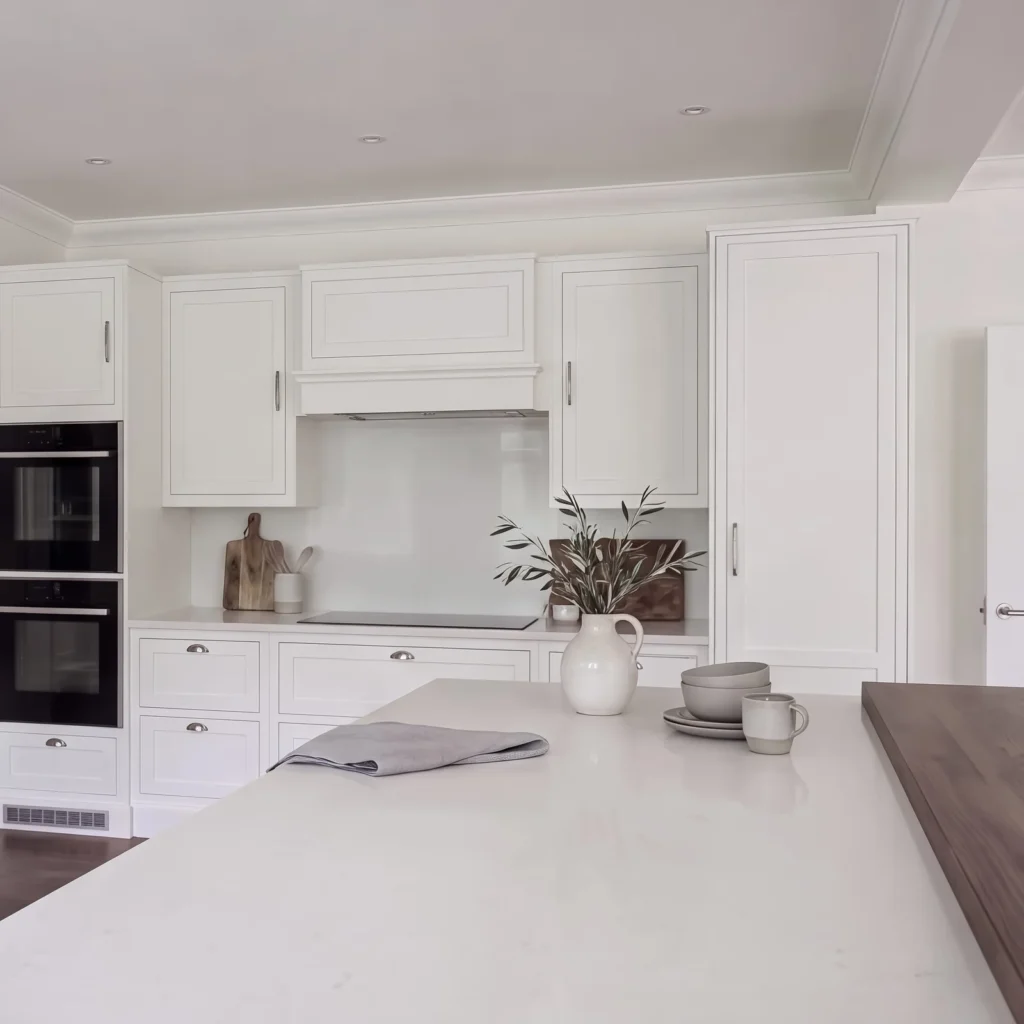 Pale grey in-frame kitchen with a white island, double ovens and a walnut worktop end