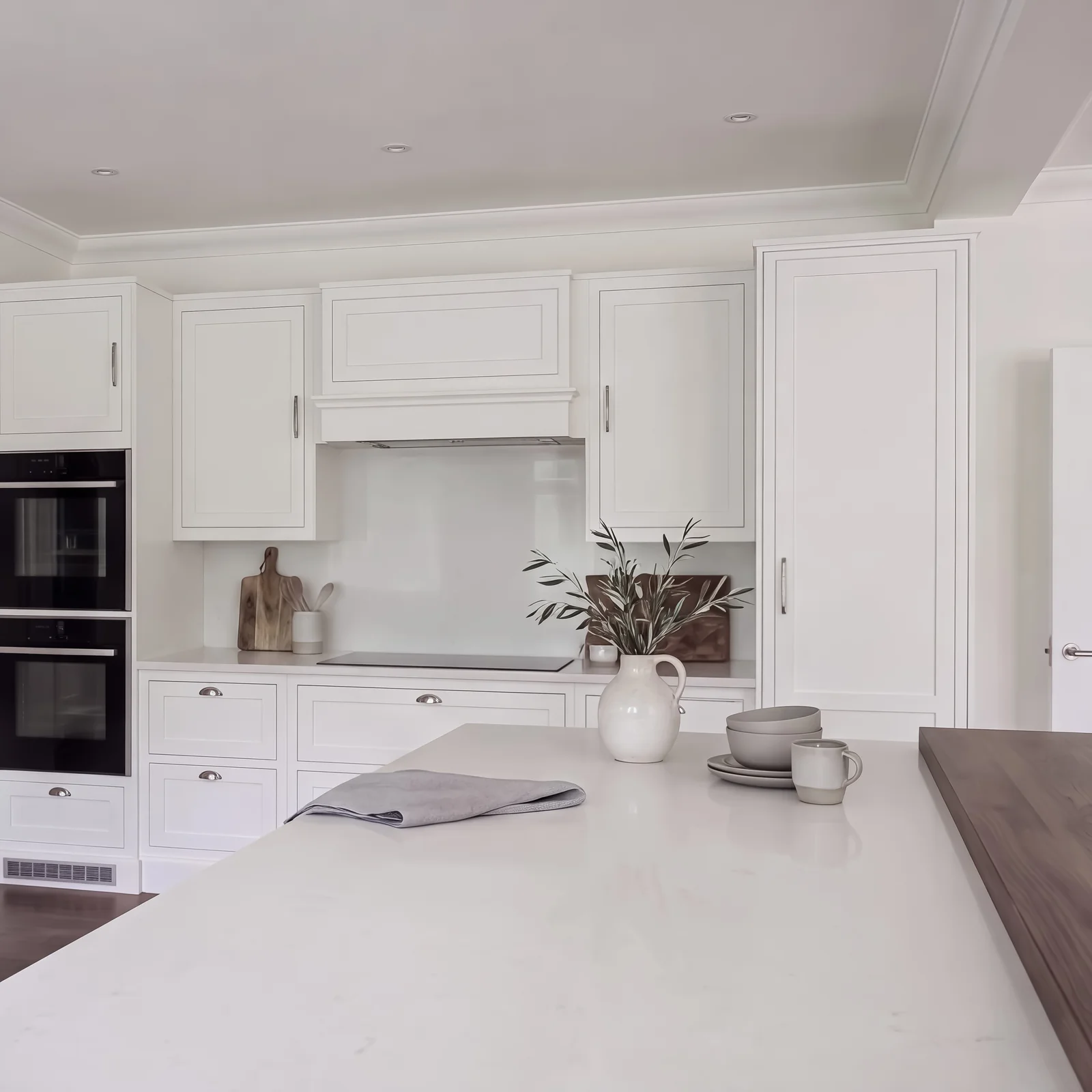 Pale grey in-frame kitchen with a white island, double ovens and a walnut worktop end