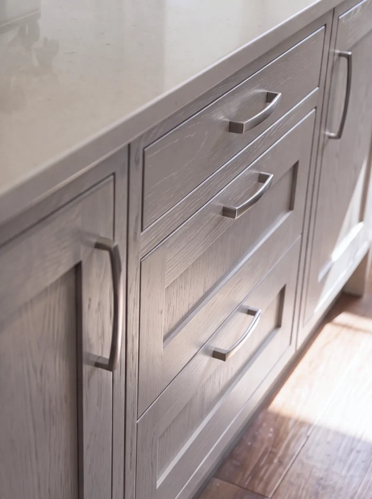 Close-up of pale grey shaker drawers with silver cup handles and a bar pull