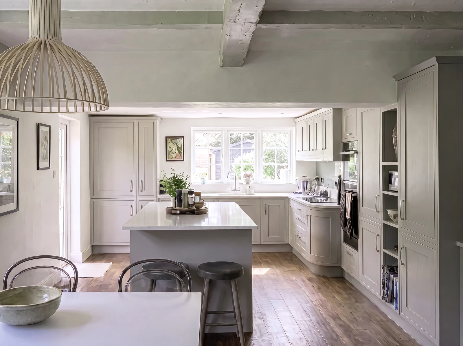 Pale grey shaker kitchen seen from the dining table, with a central island and wooden beams