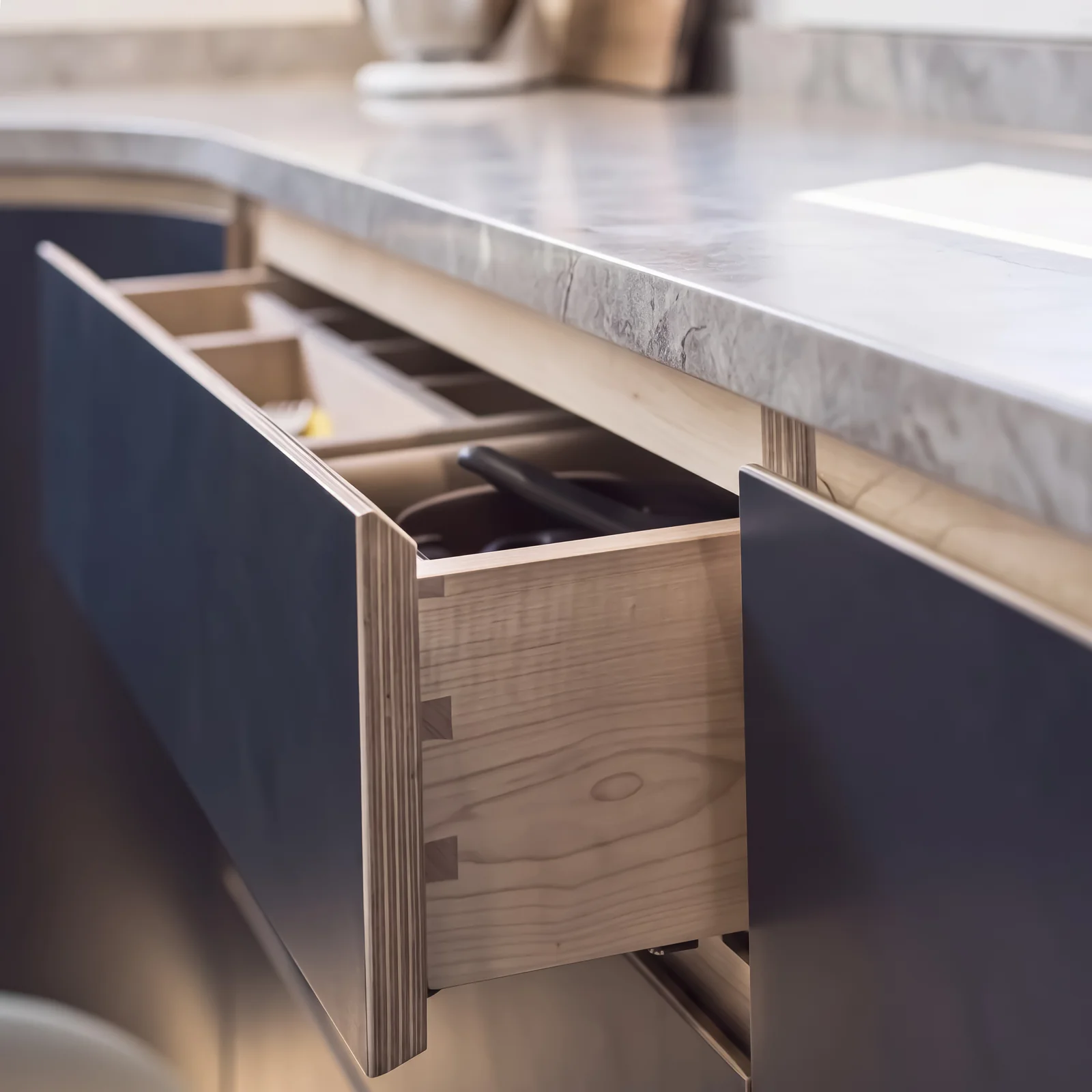 Open birch plywood drawer with dovetail joints in a navy unit under a stone worktop