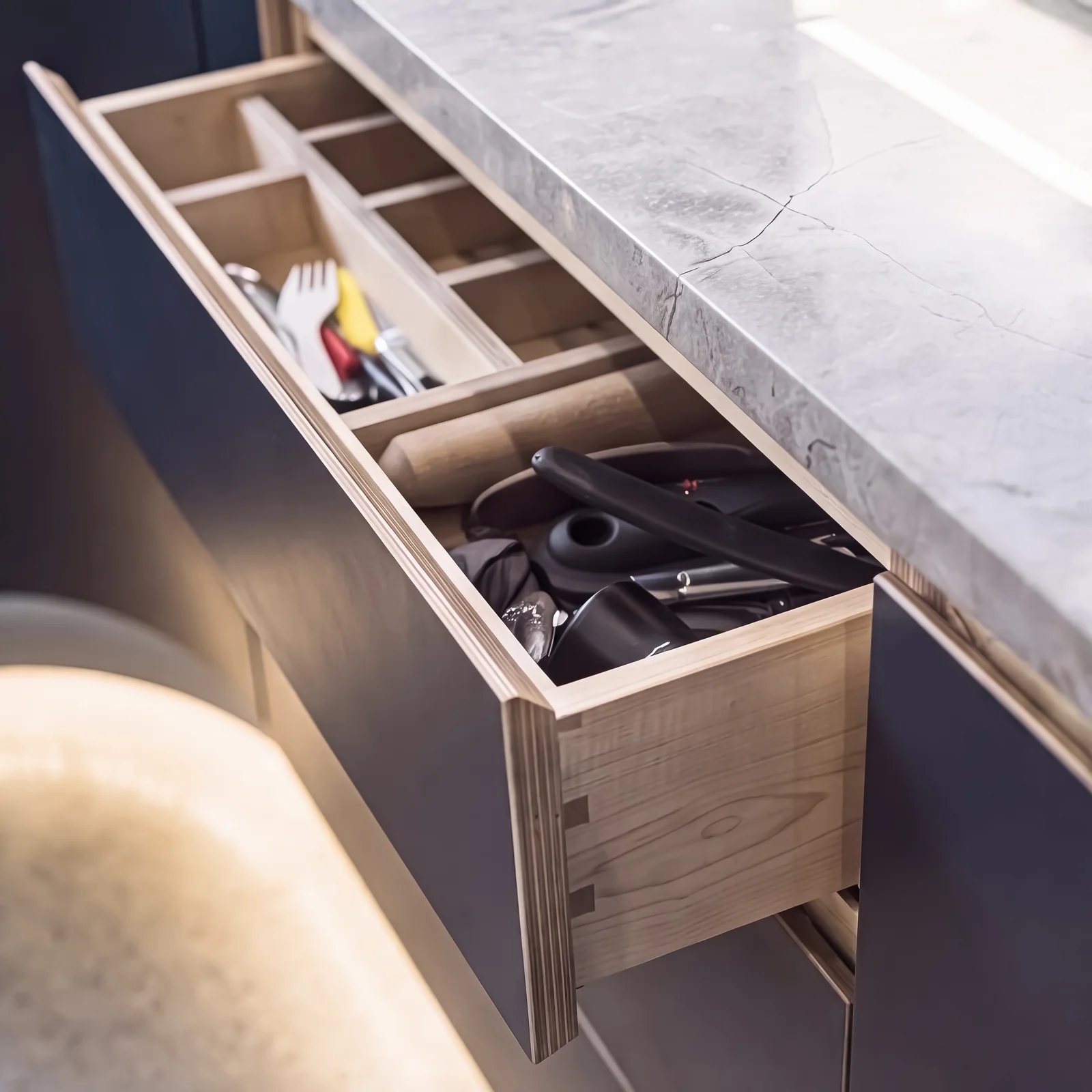 Lit birch ply cutlery drawer in a navy unit beneath a grey stone worktop