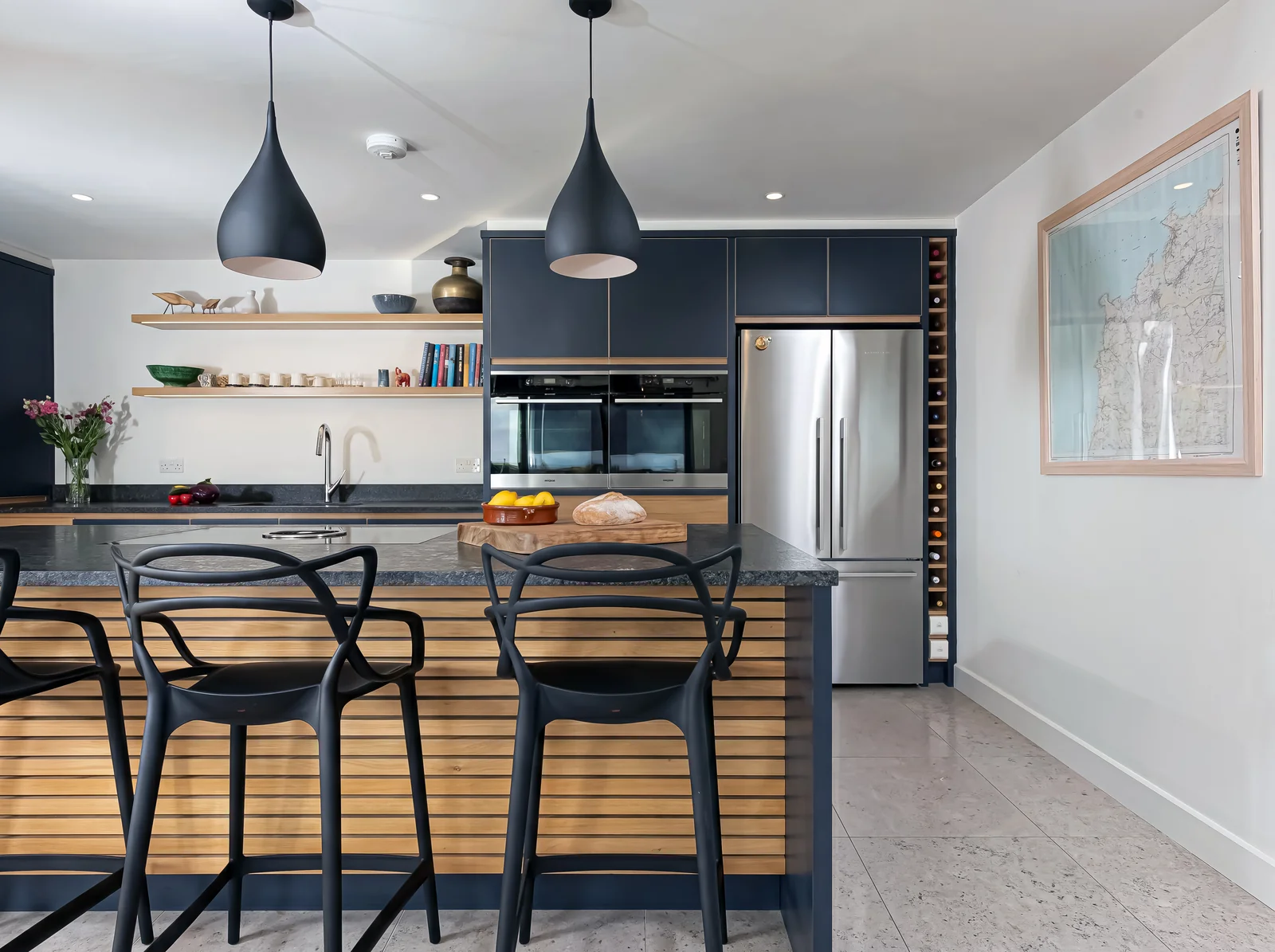 Navy island with oak slat panelling and black bar stools in front of a stainless steel fridge