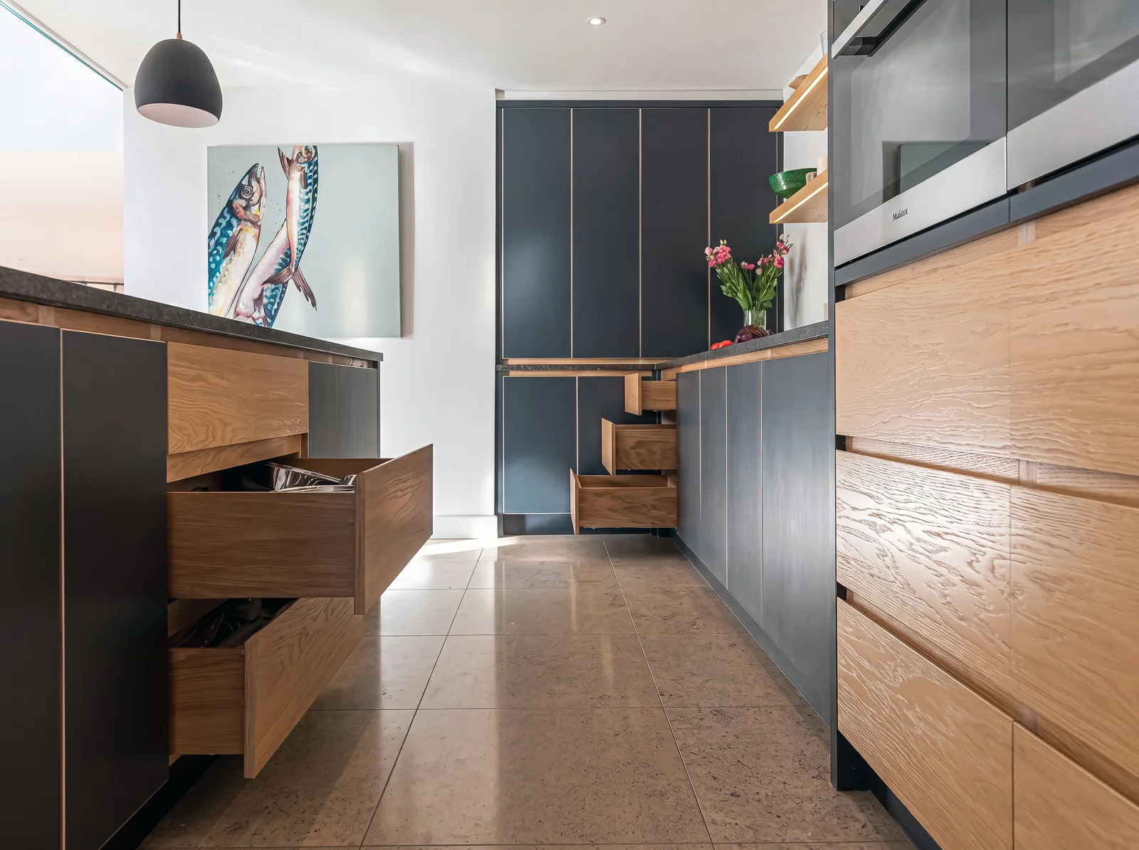 Open oak drawers in a navy and oak kitchen with black granite worktops