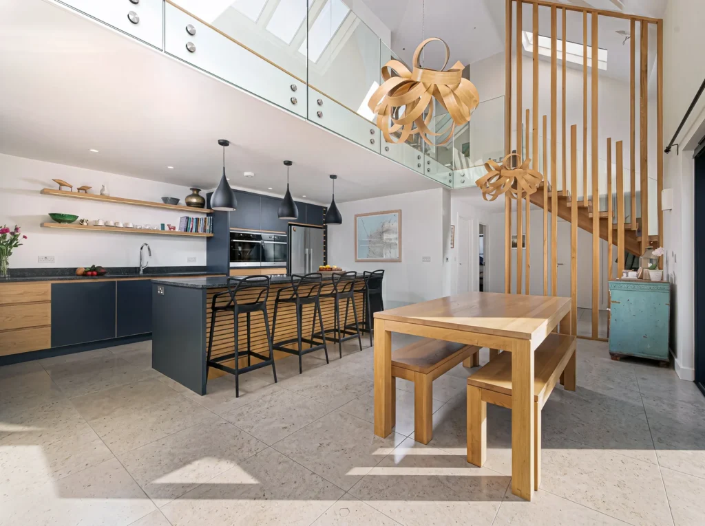 Open-plan navy and oak kitchen beside an oak dining table and a slatted oak staircase screen