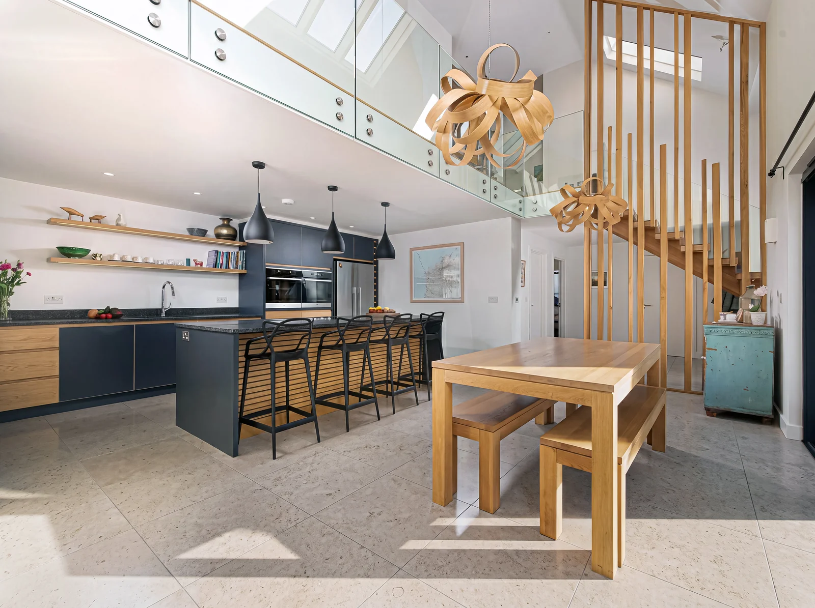 Open-plan navy and oak kitchen beside an oak dining table and a slatted oak staircase screen