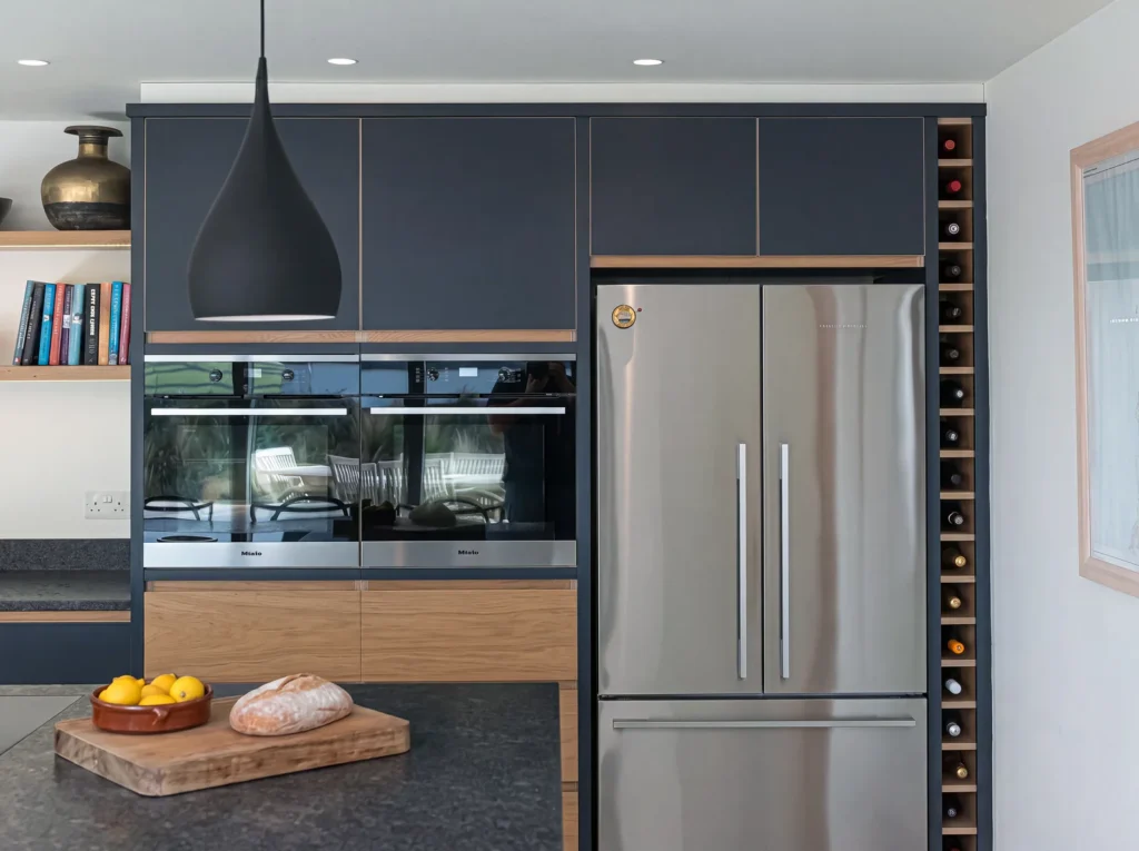 Navy wall units over built-in ovens, an oak drawer and a slim wine rack beside the fridge