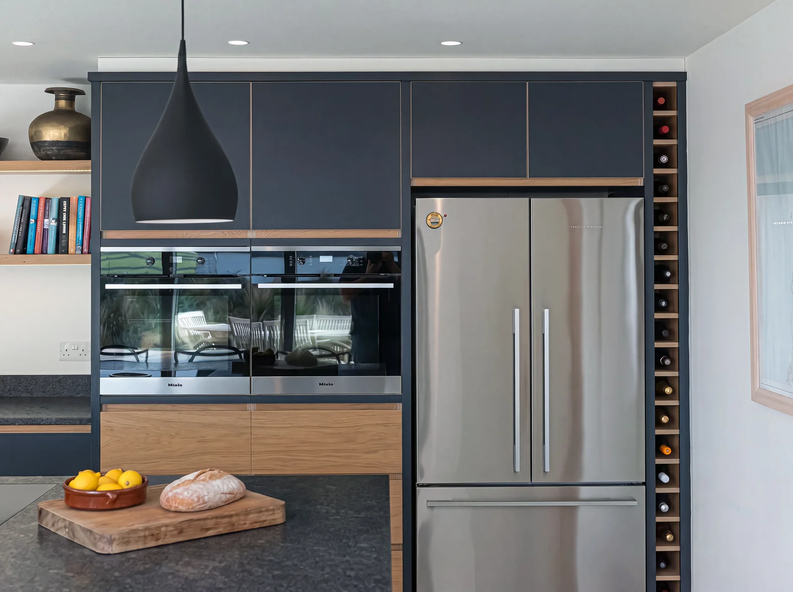 Navy wall units over built-in ovens, an oak drawer and a slim wine rack beside the fridge