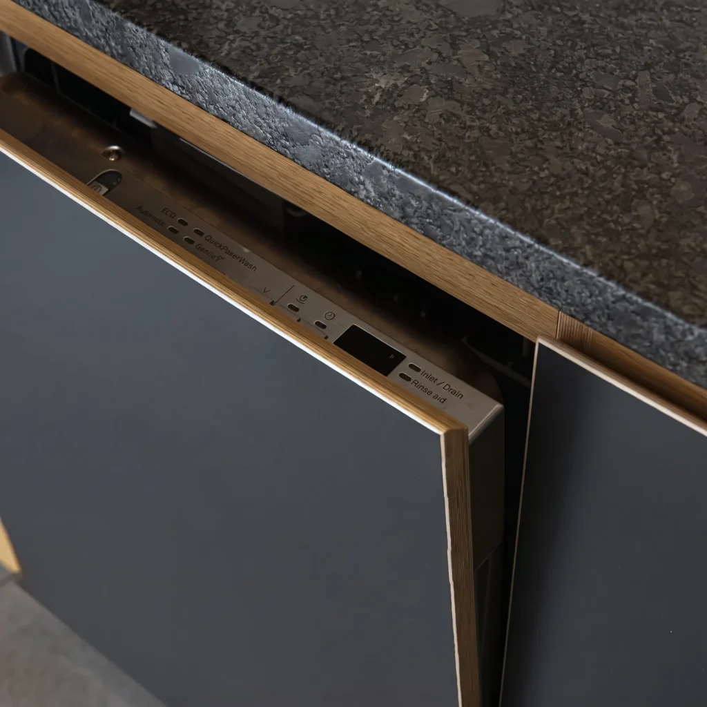 Close-up of a navy door with an oak edge beneath a leathered black granite worktop