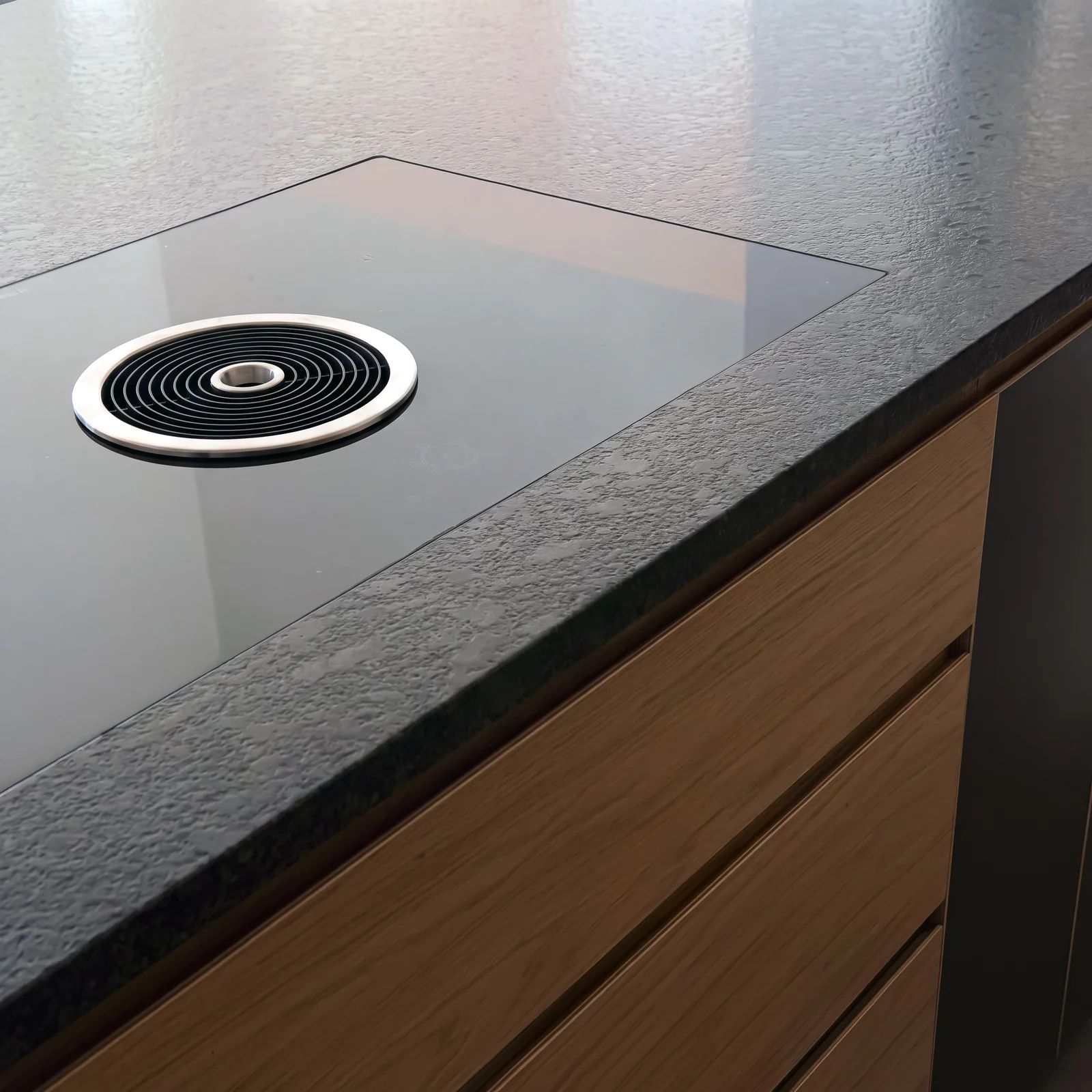 Close-up of a granite worktop with a pop-up extractor above oak drawer fronts