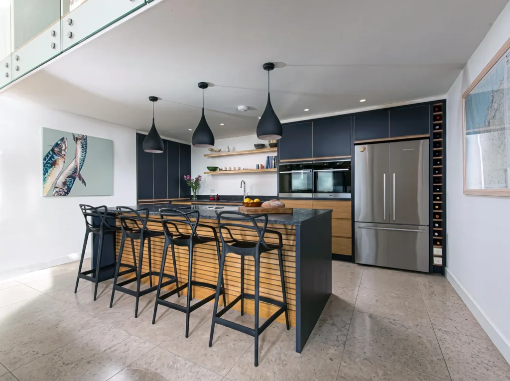 Navy kitchen island with black stools and pendant lights below a glass balcony