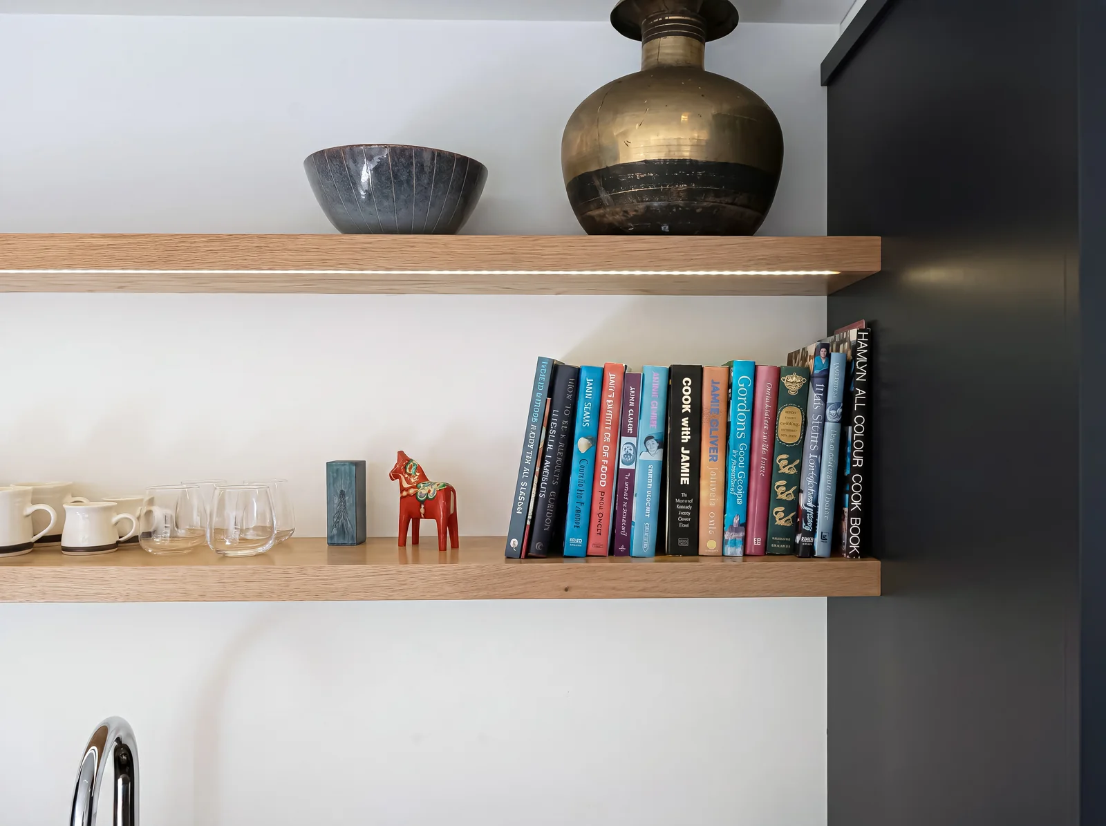 Floating oak shelves with cookbooks, a brass vase and ceramics against a white wall