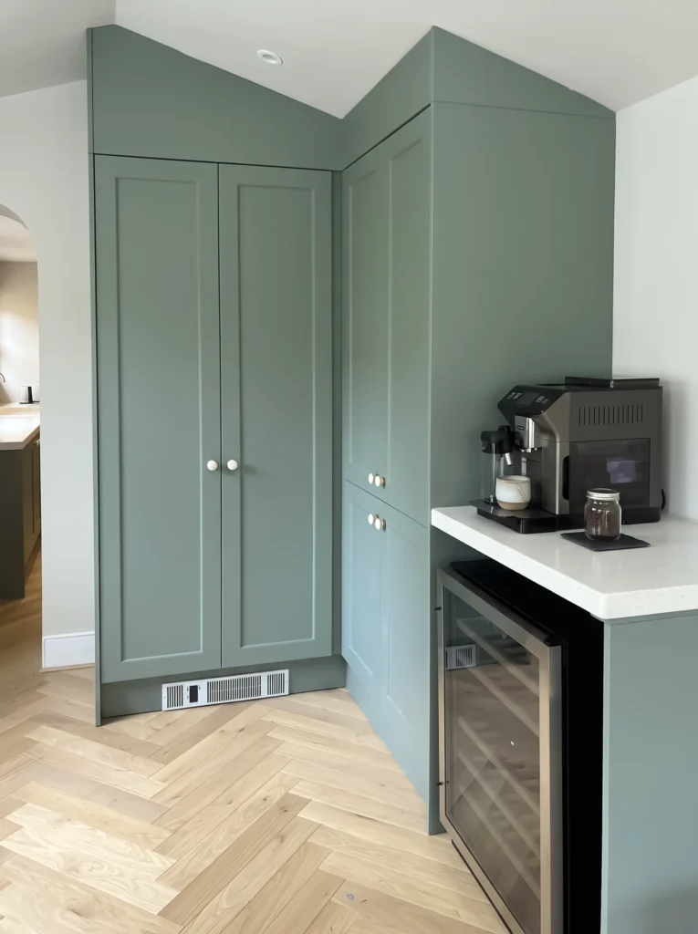 Tall sage shaker cupboards beside a coffee station with an integrated wine cooler