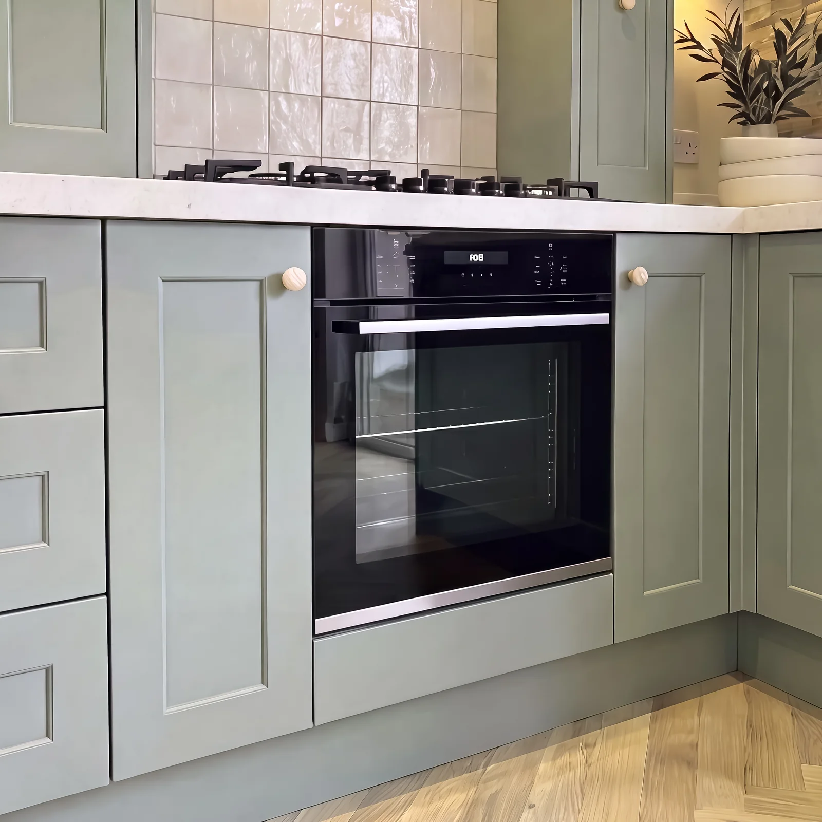 Sage shaker cabinets around a built-in oven beneath a gas hob and handmade tiles