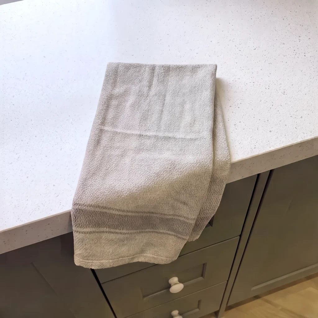 Close-up of a grey towel draped over a white quartz worktop edge above sage drawers