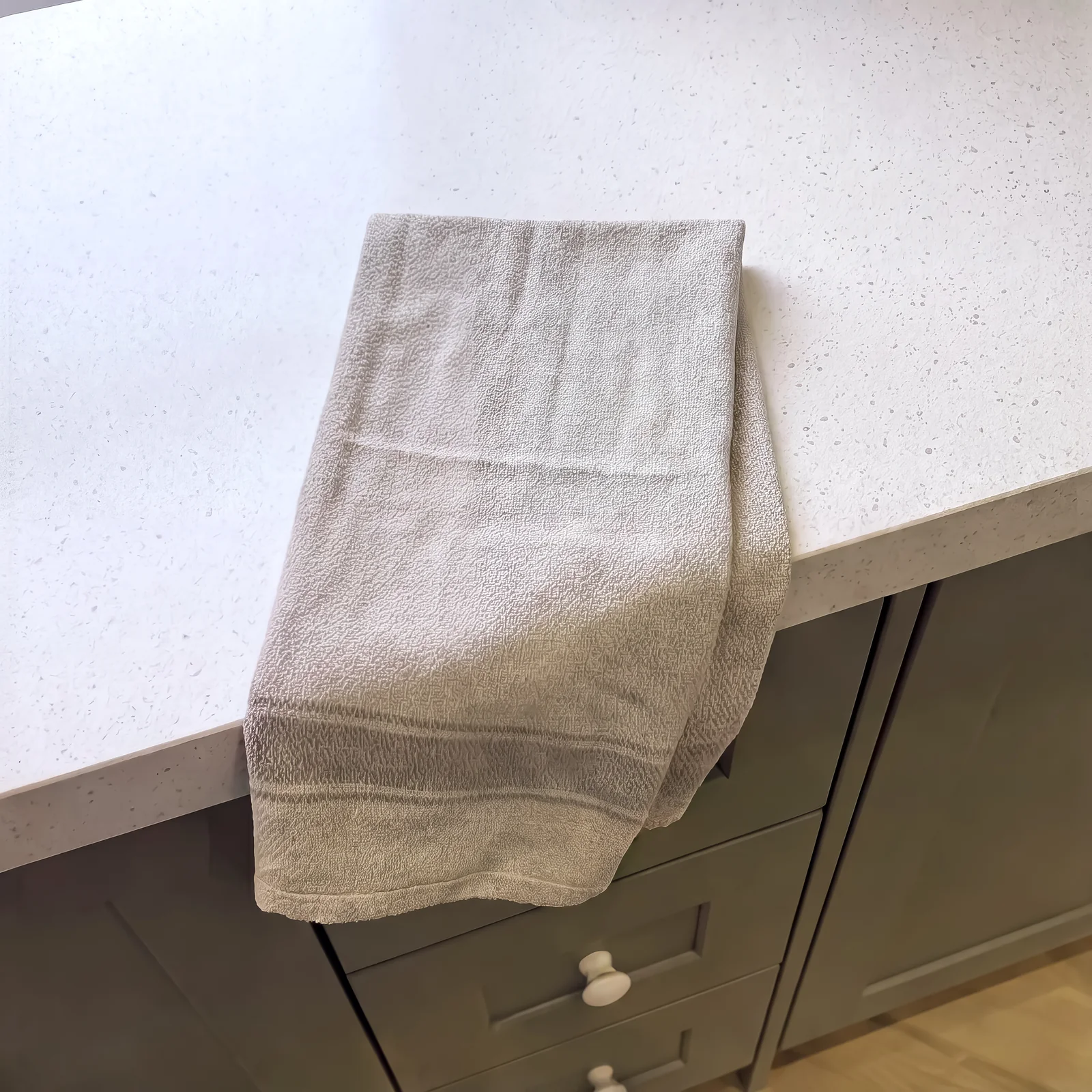 Close-up of a grey towel draped over a white quartz worktop edge above sage drawers