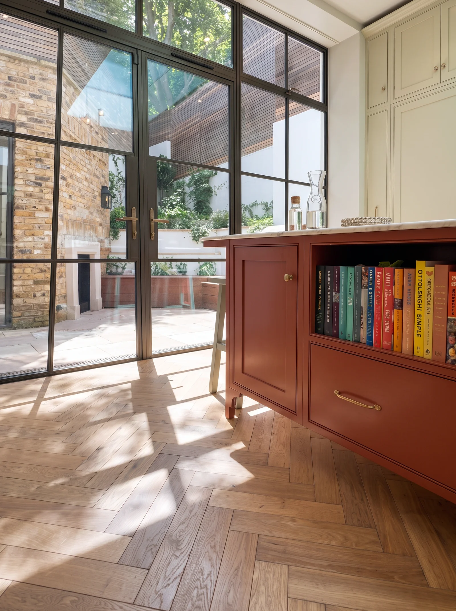 Deep red island with colourful cookbooks beside black steel-framed garden doors