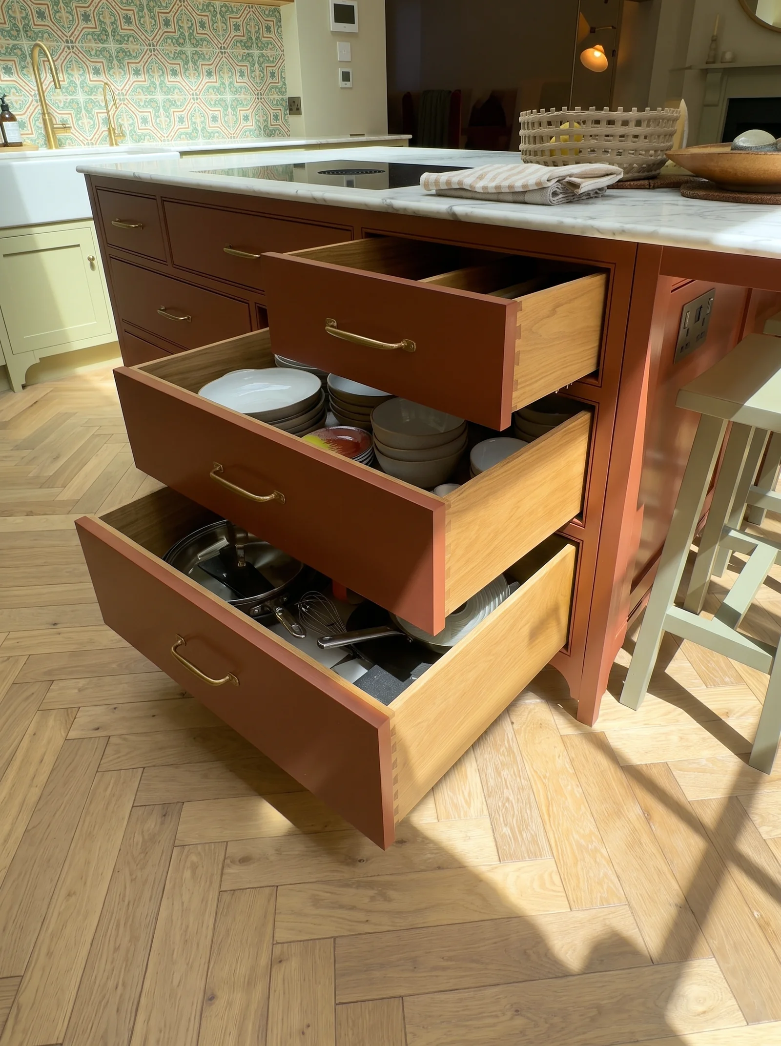 Open deep red island drawers holding pans and utensils under a marble worktop
