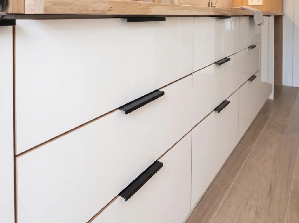 Close-up of white drawer fronts with black bar handles along a kitchen run